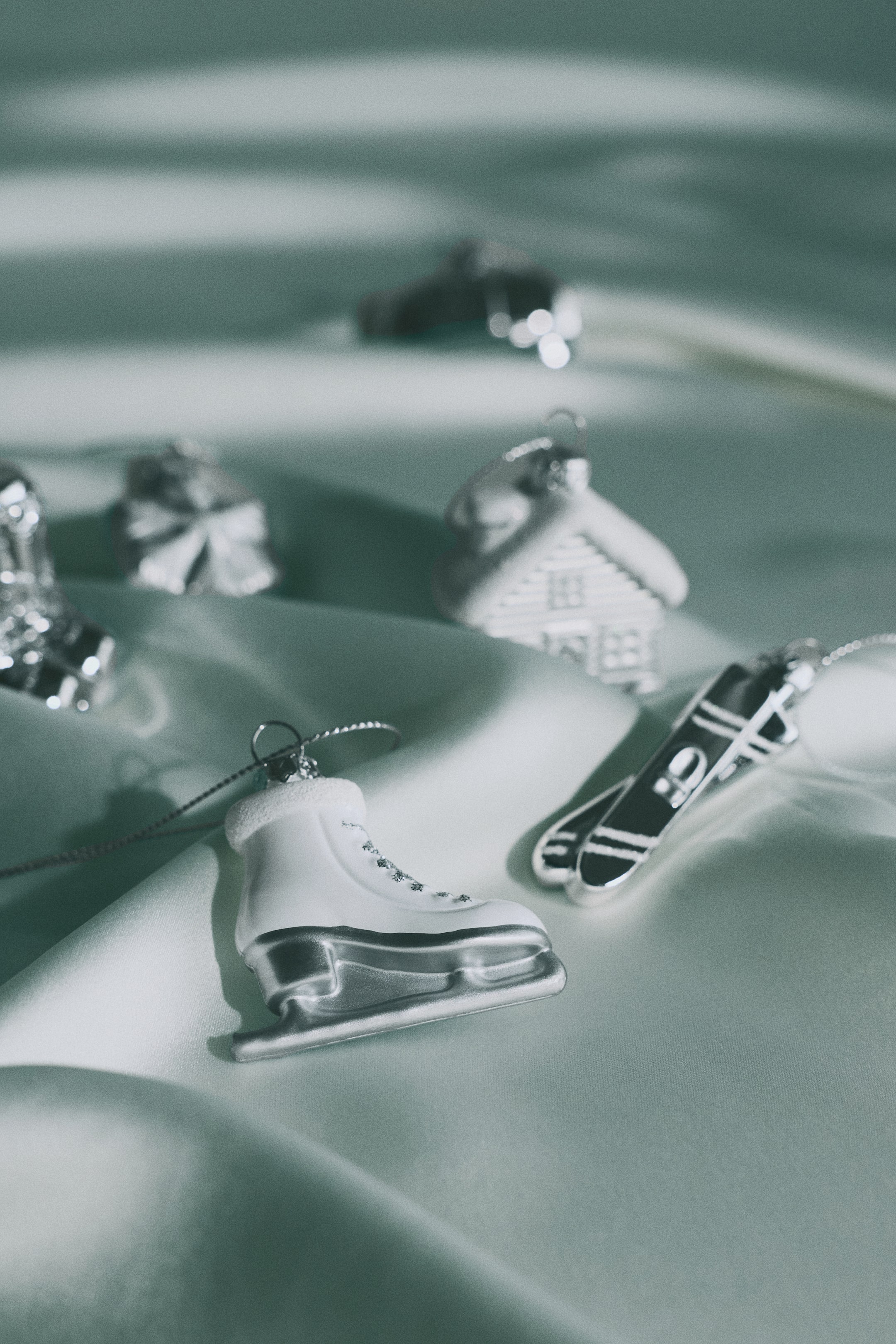 View larger image: Assorted plastic Christmas decorations are displayed in winter-themed shapes, including a white ice skate with a silver-coloured blade, a pair of silver skis, and a textured white house. Each ornament features an eyelet at the top with a thin, glittery cord for hanging.