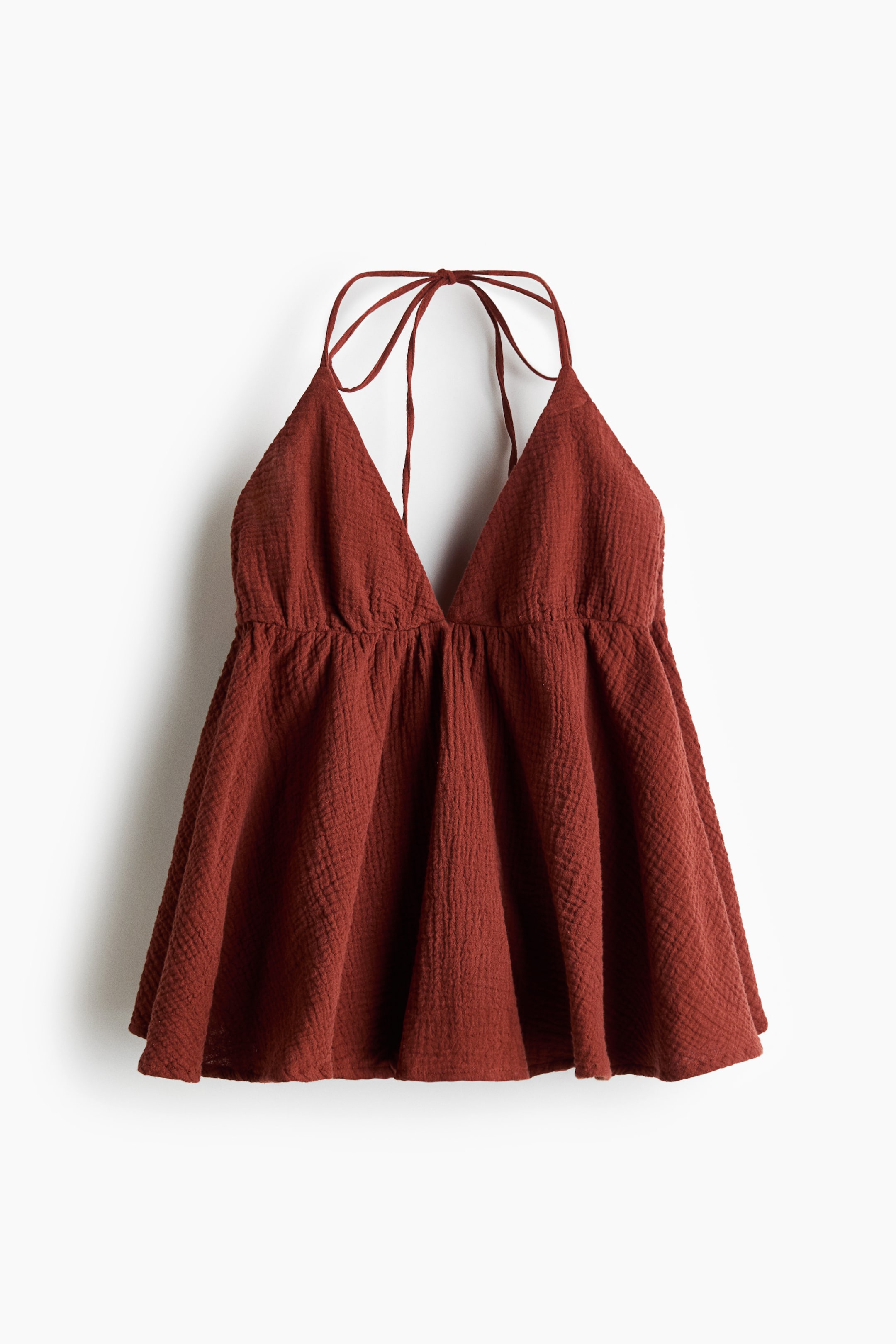 View larger image: A rust-coloured halter top is shown from the front, featuring a deep V-neck and thin tie straps knotted at the back. It is styled with an empire waist, gathered below the bust, and a flared body, all showcasing a crinkled texture.
