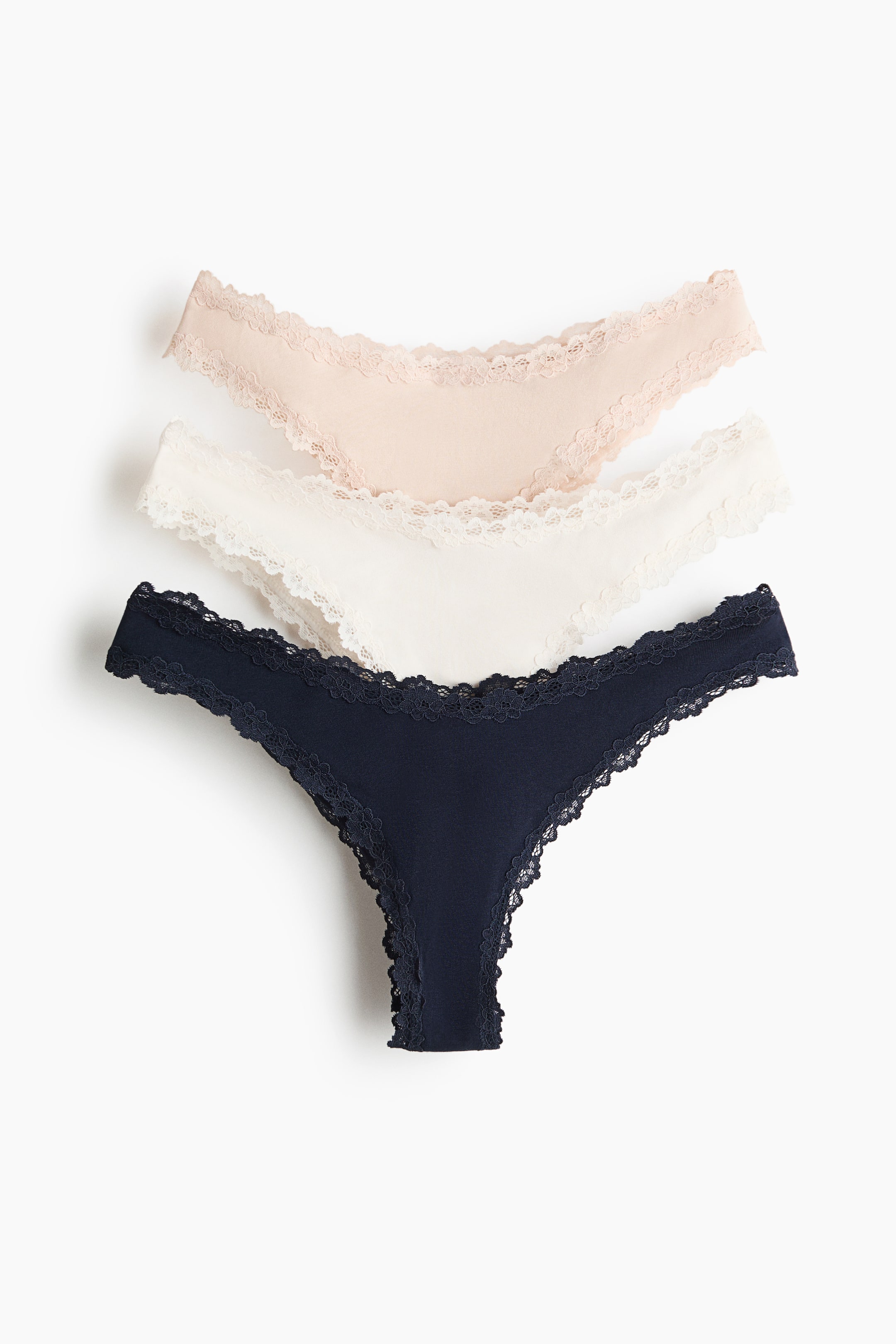 View larger image: Three thong underwear are displayed in a fanned arrangement, viewed from the front. The thongs feature lace trim along their waistbands and leg openings, and are colored nude, white, and navy.