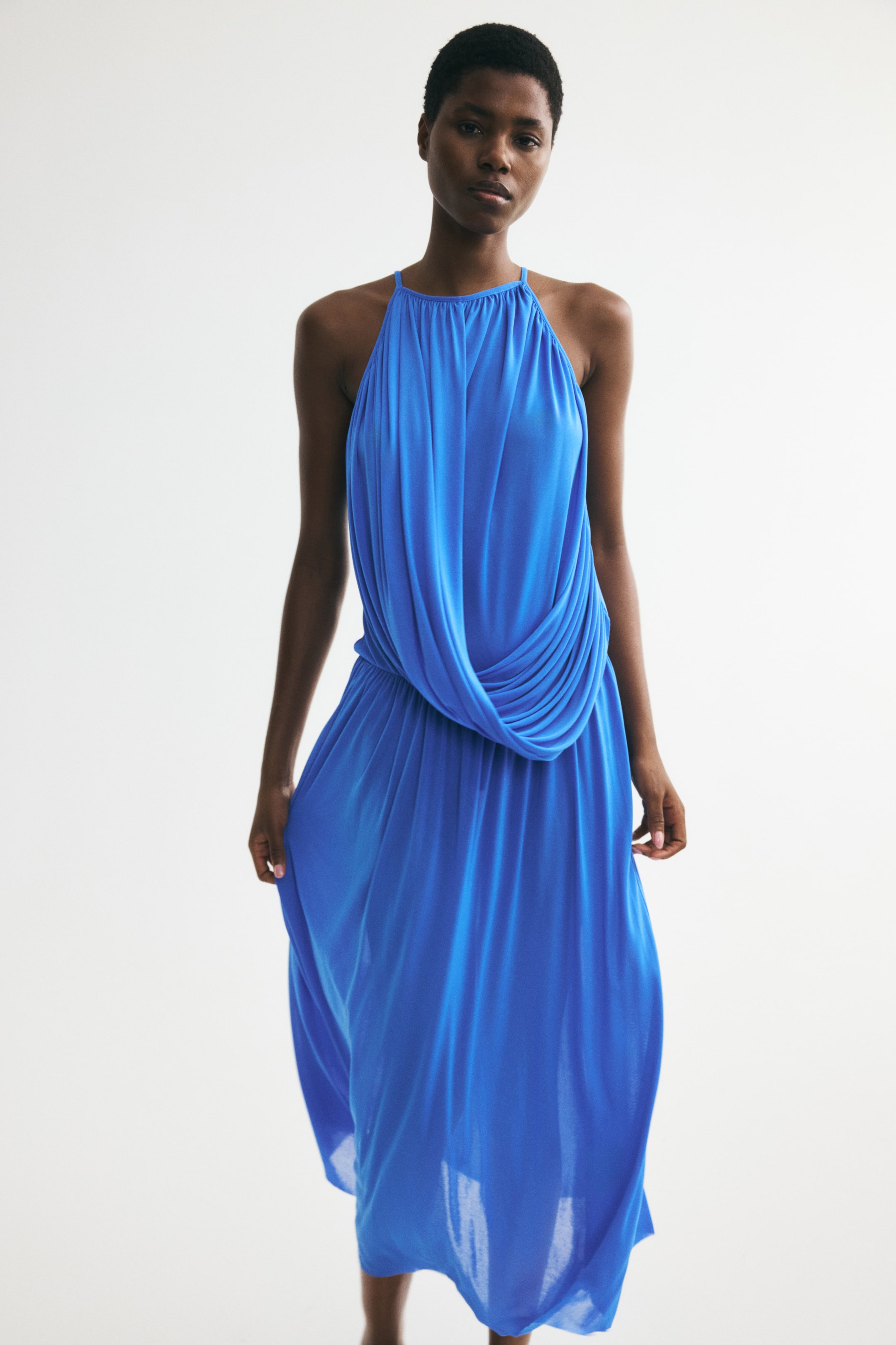 Agrandir l'image: La robe maxi bleue présente un col licou froncé et une jupe fluide, avec un drapé en forme de capuche créant un effet blouson au niveau de la taille.