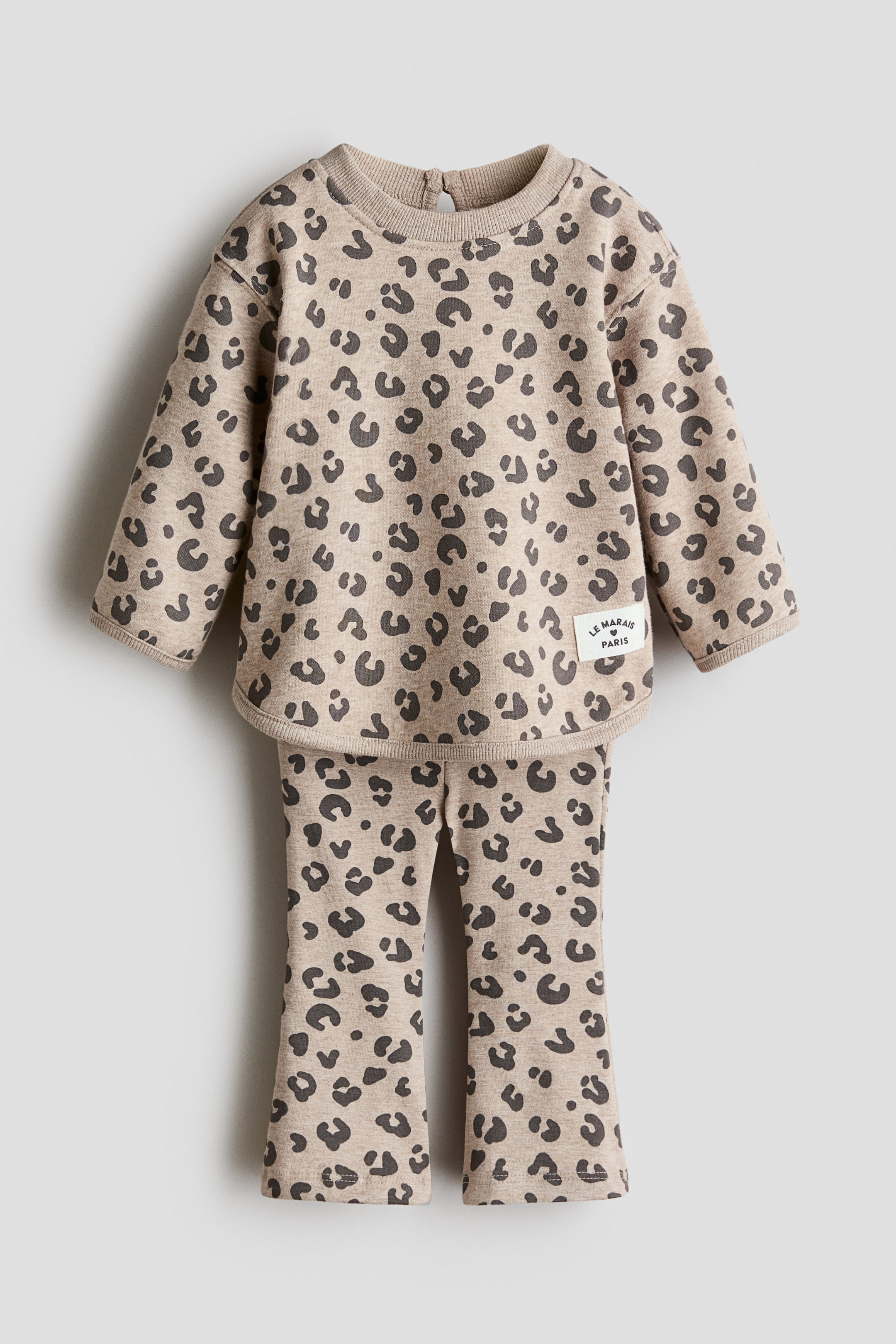 View larger image: A two-piece child's set is showcasing a beige fabric adorned with a dark leopard print, presented front-facing. The long-sleeved top exhibits a ribbed crew neck with a keyhole button closure at the back, ribbed cuffs, a rounded hem, and a small white label on the right chest. The coordinating pants feature a full-length cut with finished hems.