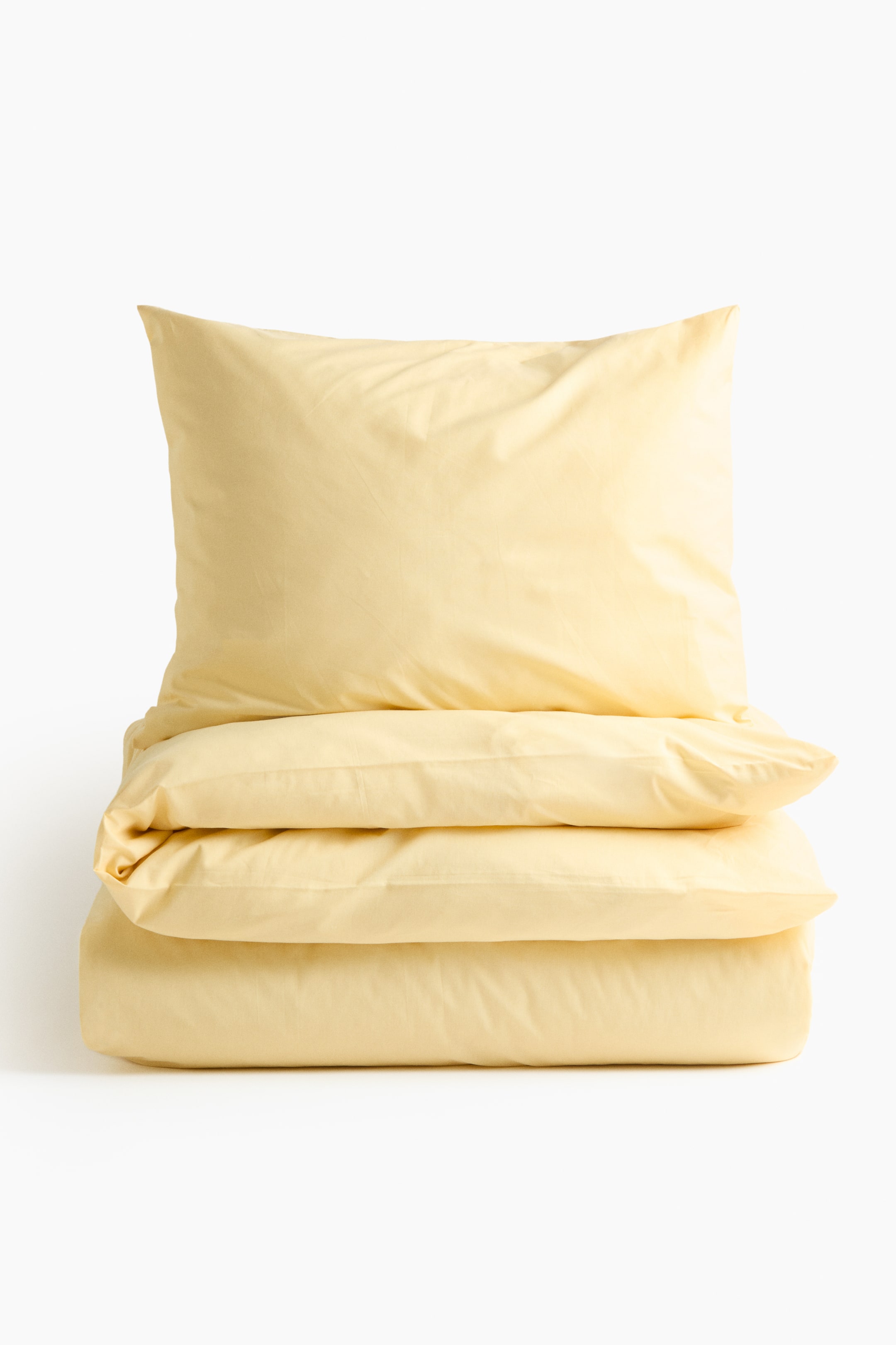 Ver imagen más grande: Un juego de funda nórdica individual de color amarillo pálido se presenta desde el FRENTE, con una funda de almohada rellena de pie sobre una funda nórdica doblada cuidadosamente. Ambos artículos muestran una textura lisa y de hilo fino.