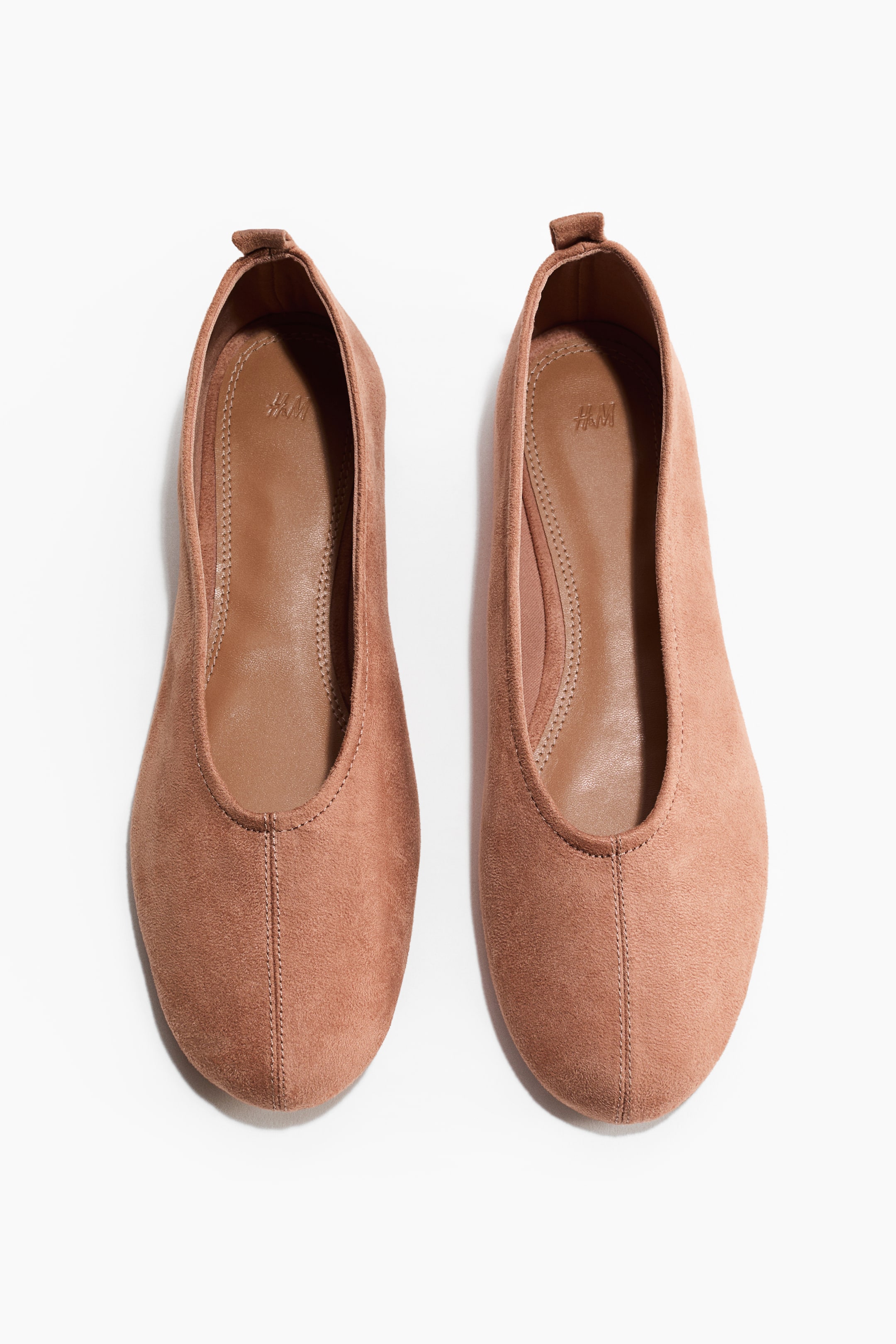 Grösseres Bild ansehen: Ein Paar gedämpft rötlich-braune Ballerinas verfügt über ein weiches, leicht aufgerautes Finish, abgerundete Zehen und eine sichtbare Naht, die mittig an der Vorderseite verläuft. Jeder Schuh zeigt zudem eine kleine Lasche an der Rückseite, und ein Jersey-Futter ist im Inneren sichtbar.