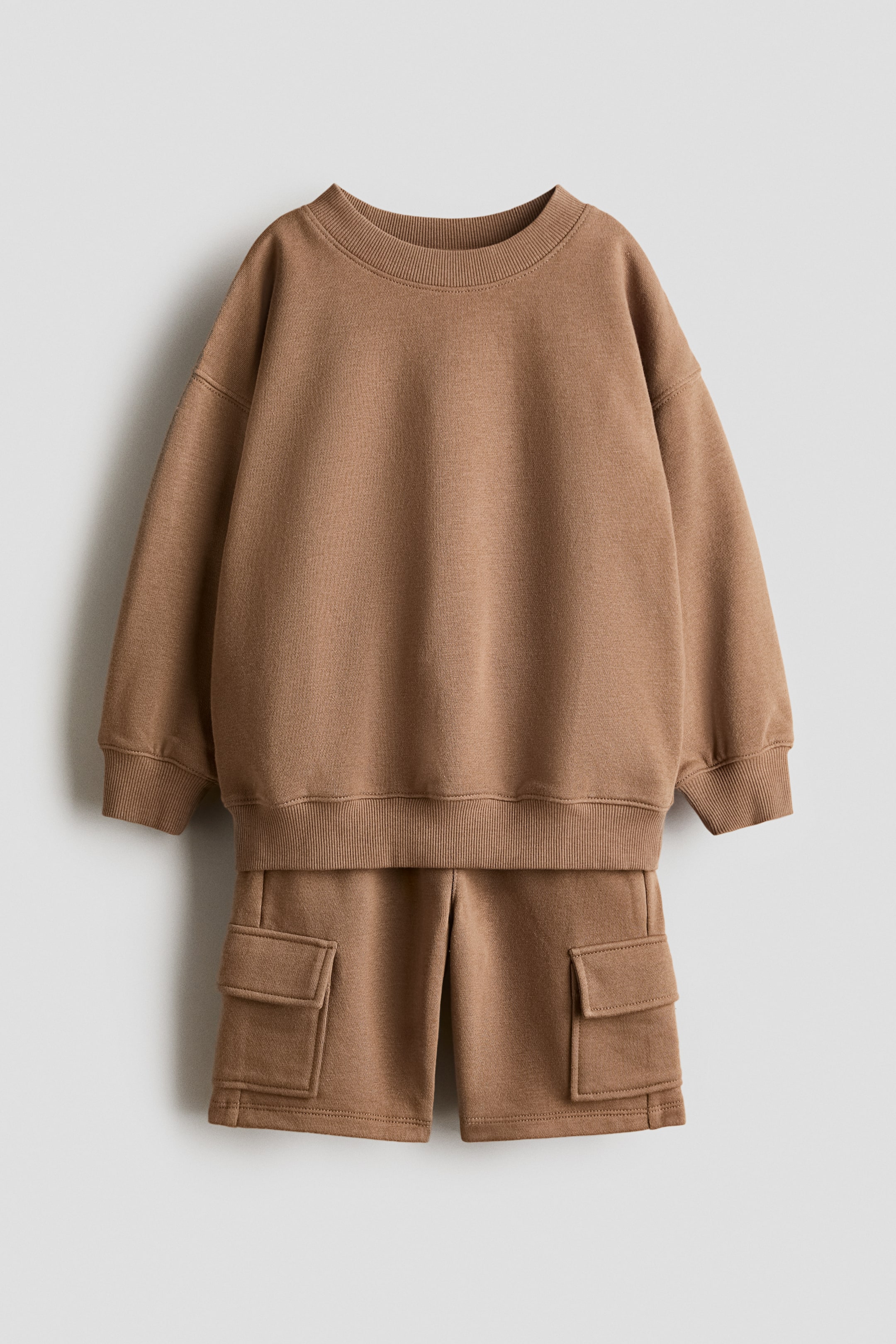 Agrandir l'image: Un ensemble deux pièces brun est présenté de face, composé d'un sweat-shirt à col rond et d'un short cargo assorti, tous deux en jersey doux. Le sweat-shirt présente des poignets et un ourlet côtelés, et le short est pourvu de poches à rabat sur chaque jambe.