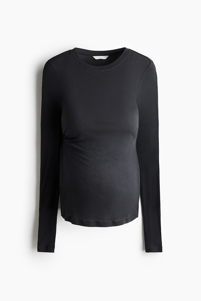 A black long-sleeve maternity top is shown from the front, featuring a ribbed crew neck, a fine-ribbed knit texture, and subtle side gathering designed to accommodate a maternity fit. - 1