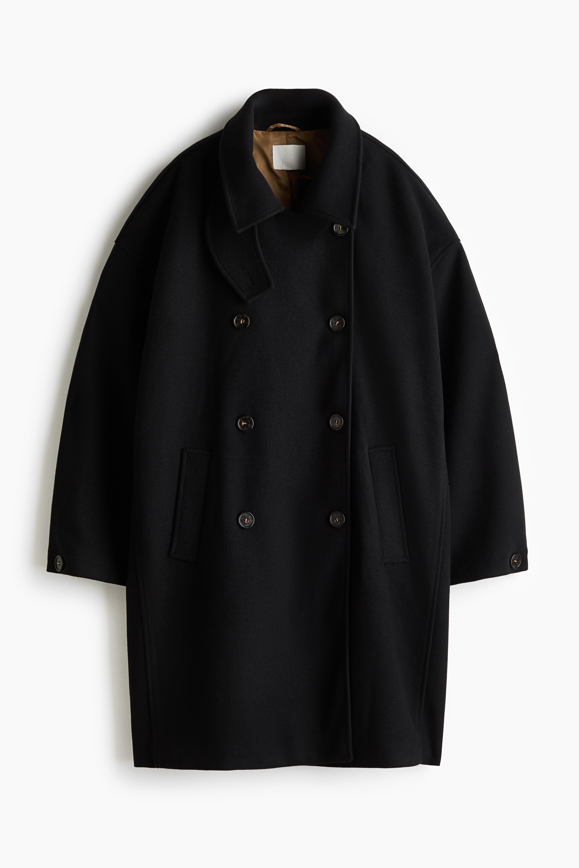A black, double-breasted coat in felted fabric is worn by the model, with her hands resting in the welt side pockets. The coat features a high open collar, front buttons and button-cuffed sleeves, and is styled with a grey knit jumper tied around the waist.