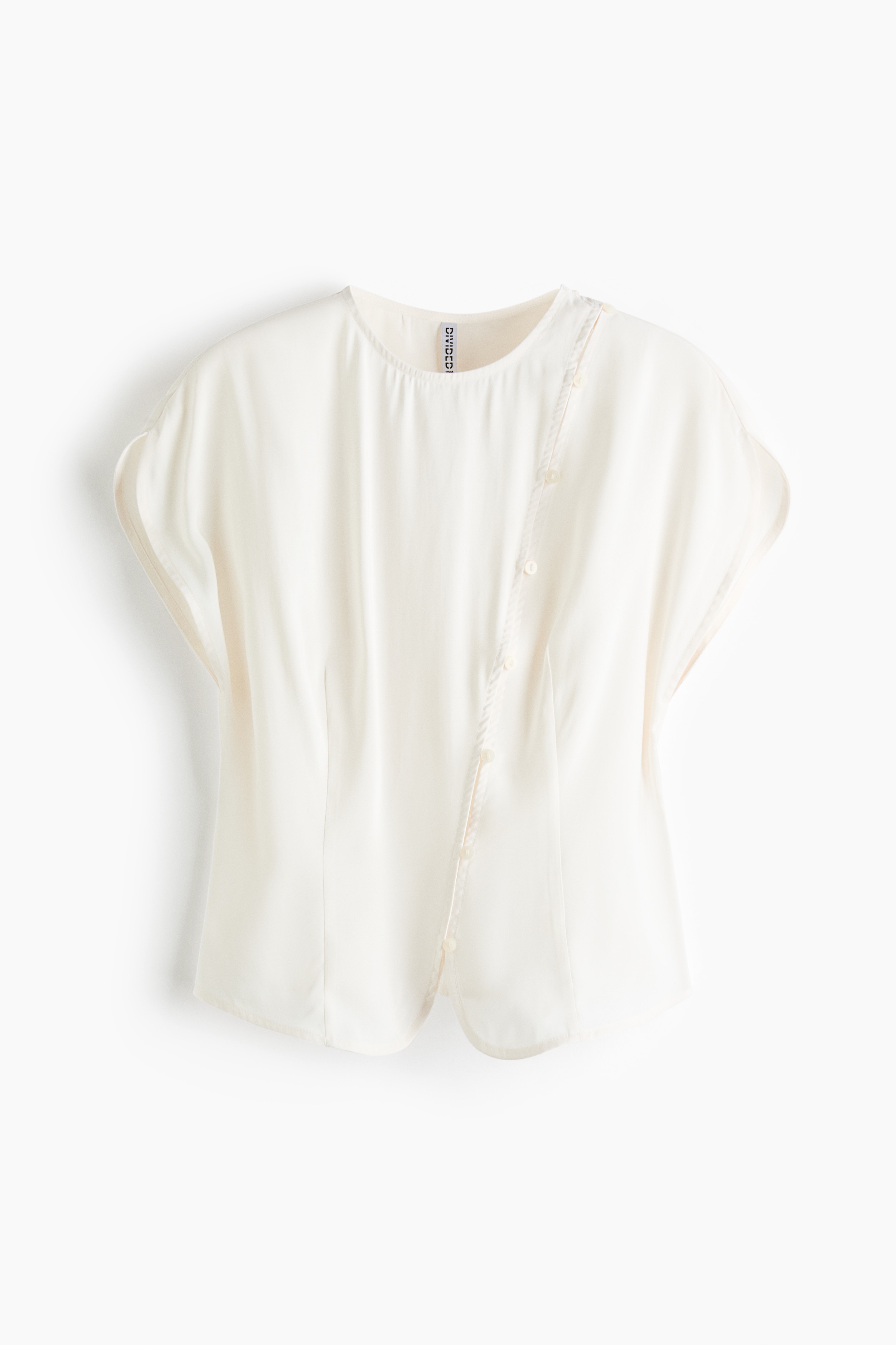 The model is wearing a cream-colored blouse featuring a round neckline, cap sleeves, and shaping waist darts. The blouse is designed with a diagonal row of button-and-loop fasteners running from one shoulder down the front.