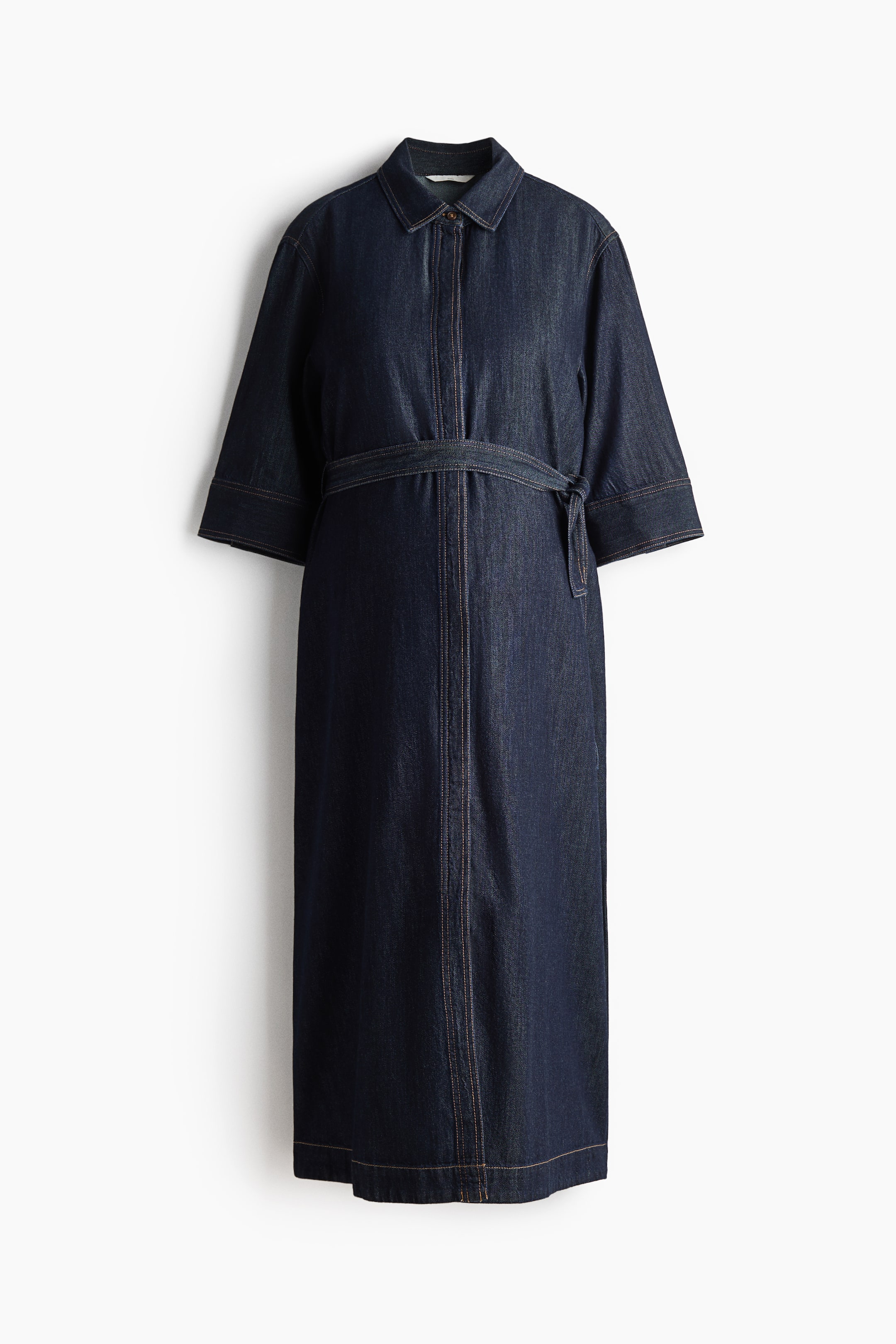 Προβολή μεγαλύτερης εικόνας: Ένα σκούρο μπλε denim φόρεμα απεικονίζεται από μπροστά, με μυτερό γιακά, πατιλέτα πλήρους μήκους και μανίκια τριών τετάρτων. Ζώνη από το ίδιο ύφασμα σφίγγει τη μέση, ενώ ραφές σε αντίθεση προσθέτουν λεπτομέρεια στο ένδυμα.