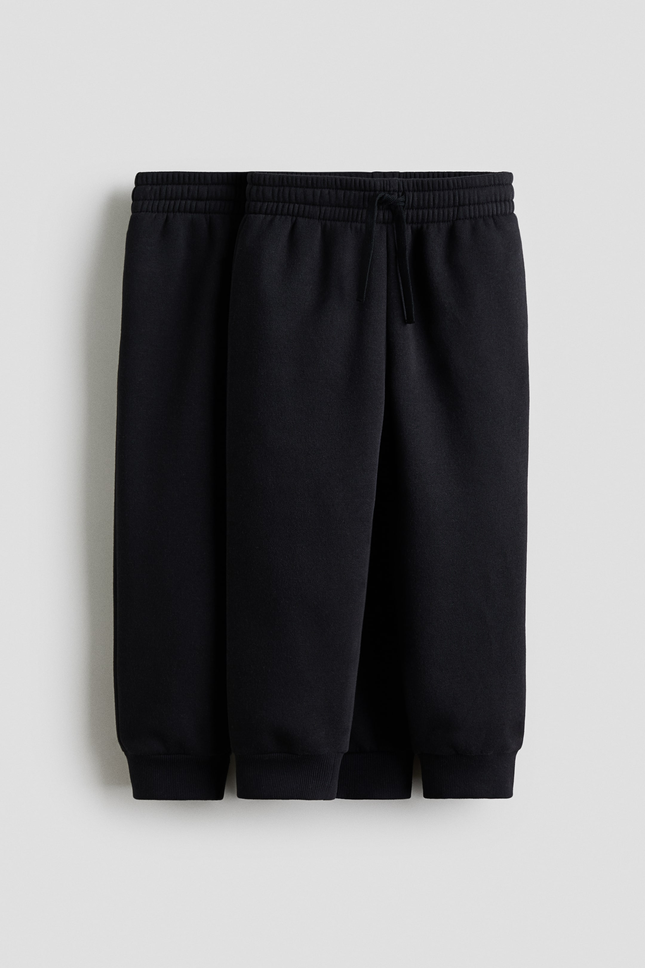 View larger image: Two pairs of black joggers are presented from a front-facing angle, featuring elasticated waistbands with a visible drawcord and ribbed cuffs.