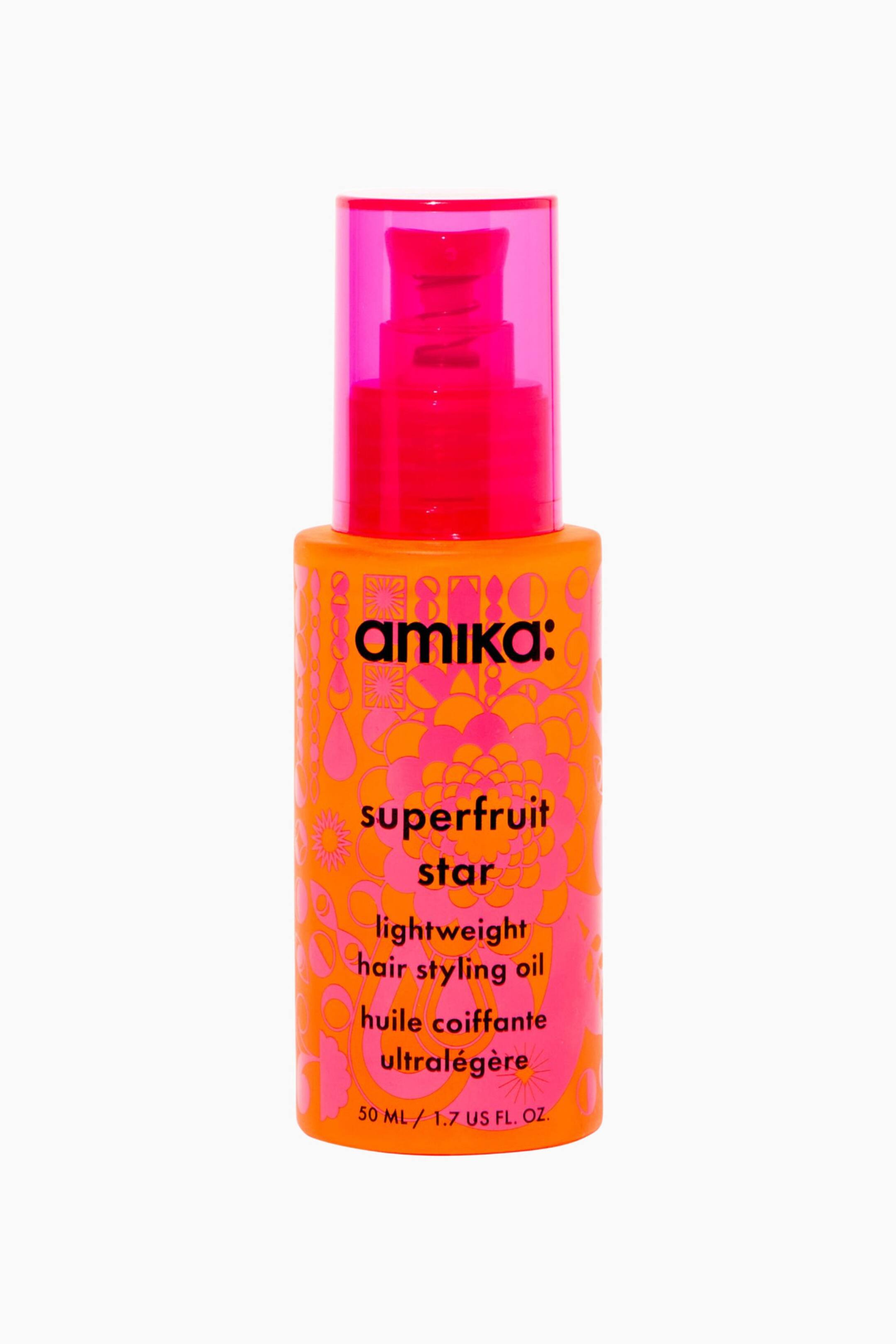 Visa större bild: En cylindrisk orange flaska med Amikas Superfruit Star Lightweight Hair Styling Oil står upprätt, vänd framåt och visar ett livfullt rosa blom- och geometriskt mönster. Flaskan har en klart rosa pumpdispenser innesluten i ett semitransparent rosa lock, med svart text som anger varumärket och produktnamnet på framsidan.