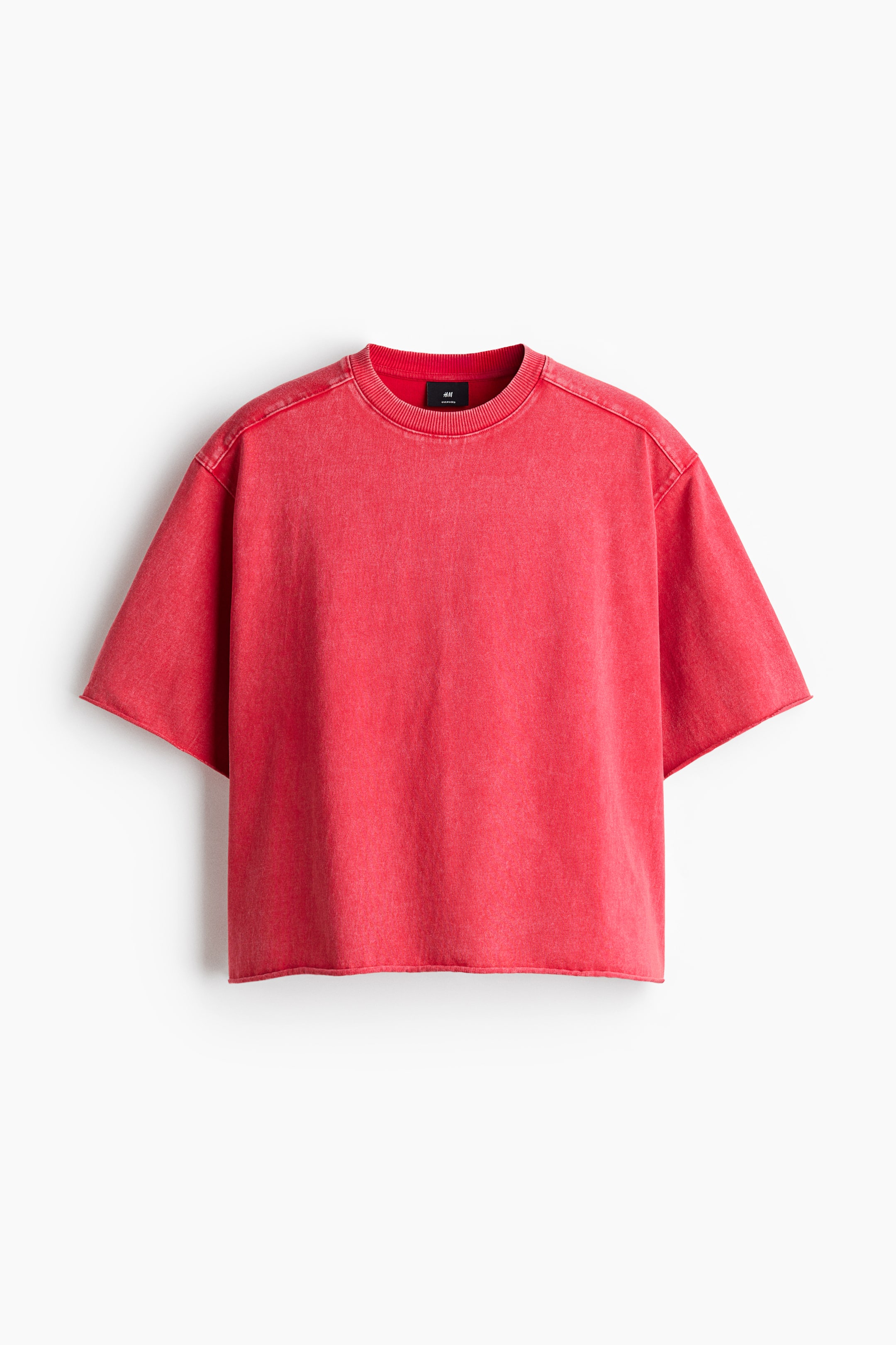 View larger image: A red boxy-style t-shirt is showcased from the front, highlighting a round, ribbed neckline, dropped shoulders, and a yoke. Raw edges are visible at the cuffs and hem, contributing to an oversized, baggy silhouette.
