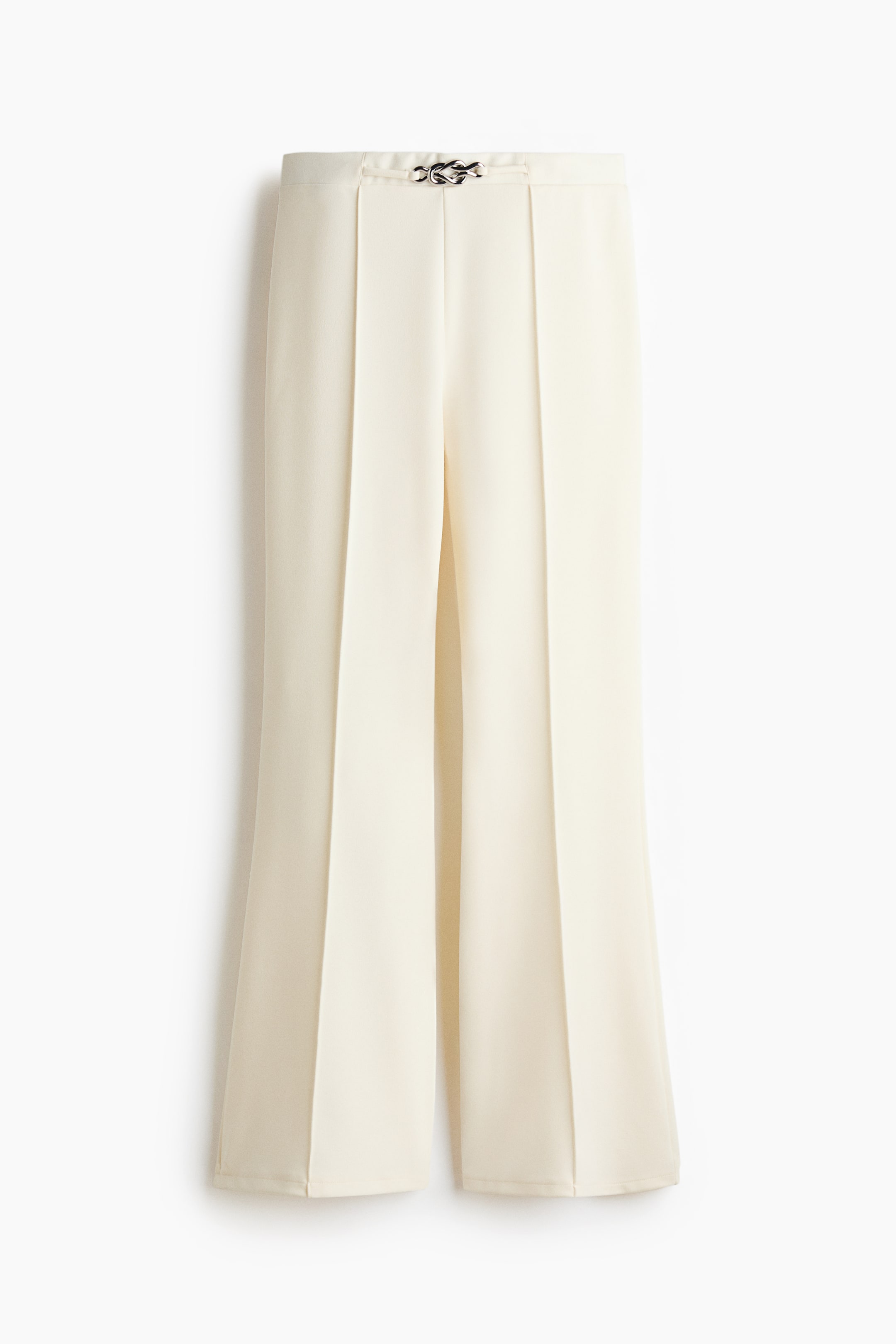 View larger image: "Cream-coloured trousers are showcased at the front, highlighting a silver-toned knot clasp at the central waist. Distinct vertical pressed creases run down the wide legs."