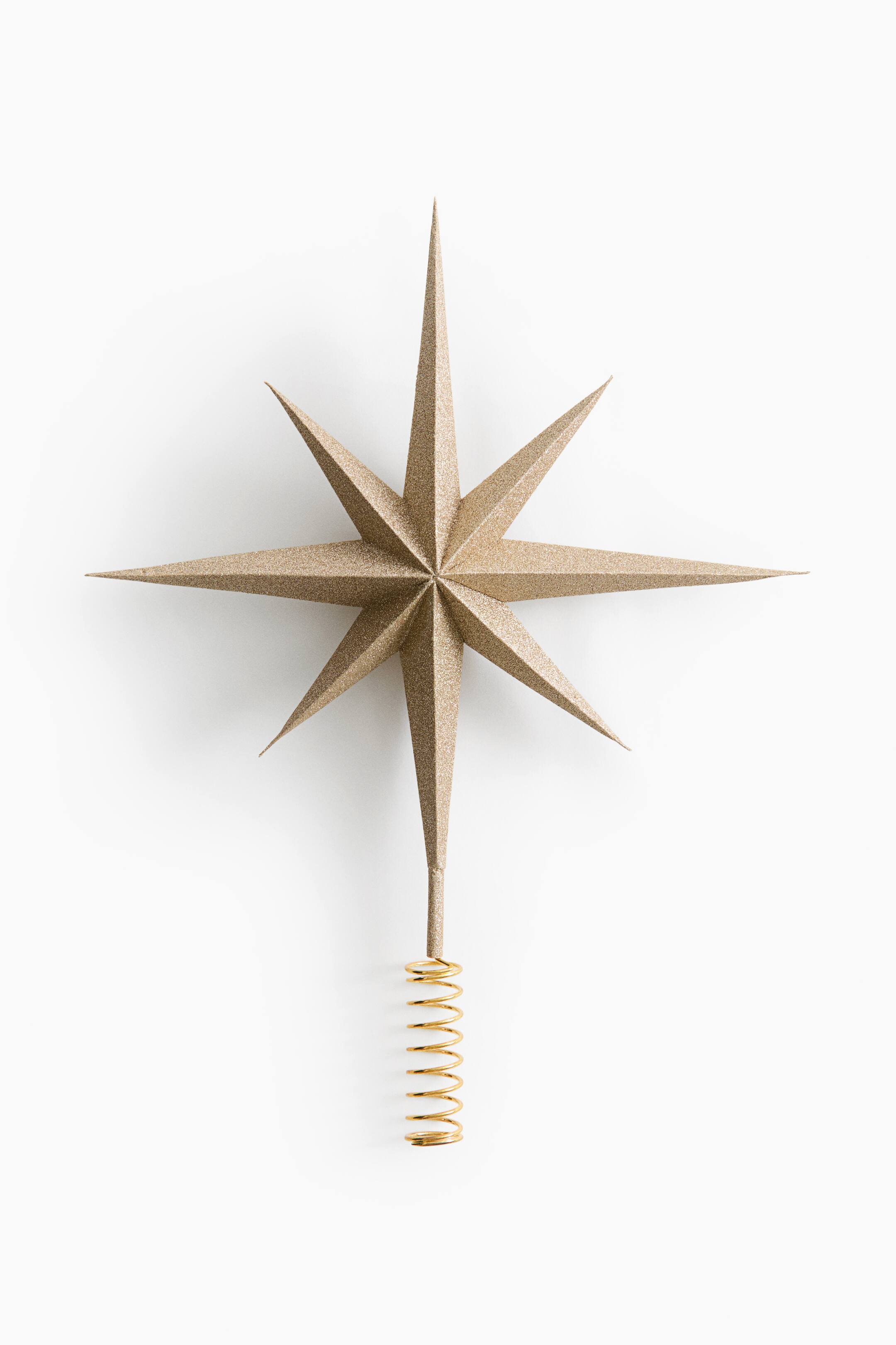 View larger image: A gold star tree topper is shown facing front, featuring a textured, glittery finish over its three-dimensional, eight-pointed faceted design. The star is connected to a gold-toned spiral wire coil base at the bottom.