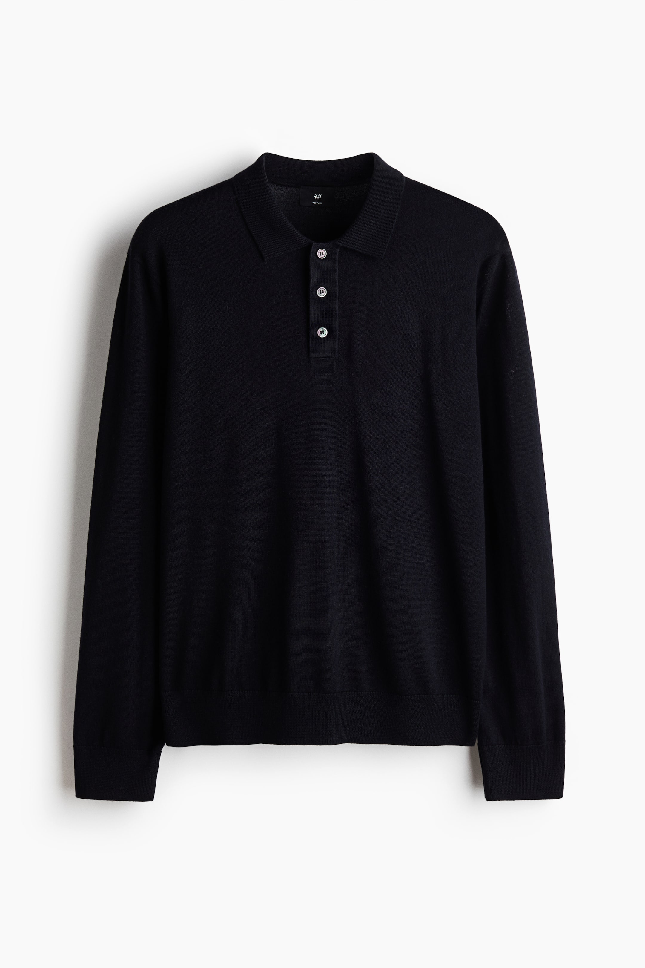 View larger image: A dark blue long-sleeve polo shirt is hanging, facing forward, featuring a classic collar and a three-button placket with light-coloured buttons. It is finished with ribbed cuffs and a ribbed hem.