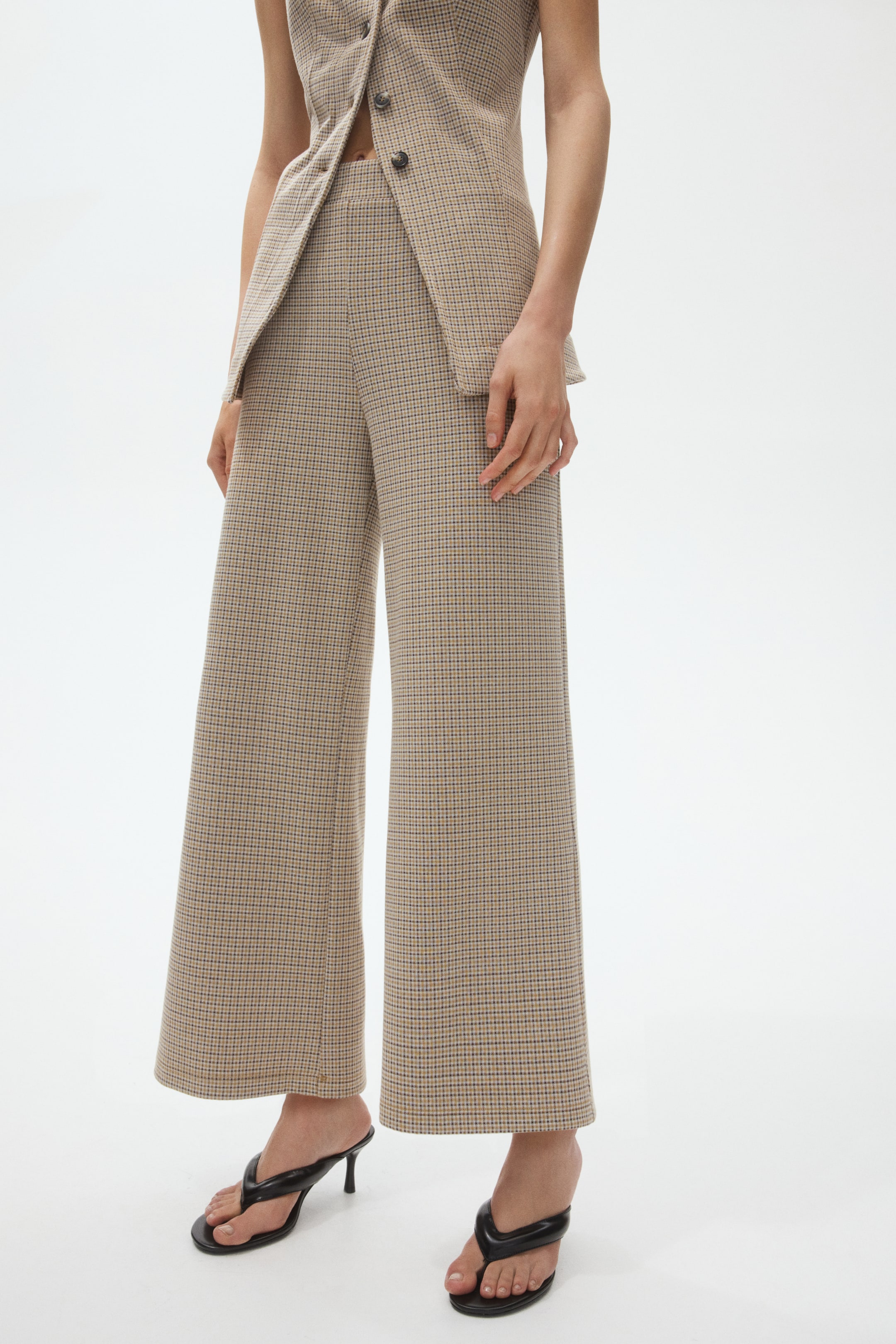 View larger image: Wide-leg trousers in a beige and blue small check pattern are displayed, facing forward. They feature a high-waisted fit and a flowing silhouette, styled with a matching vest slightly overlapping the waistband and extending to a cropped length above the ankles.