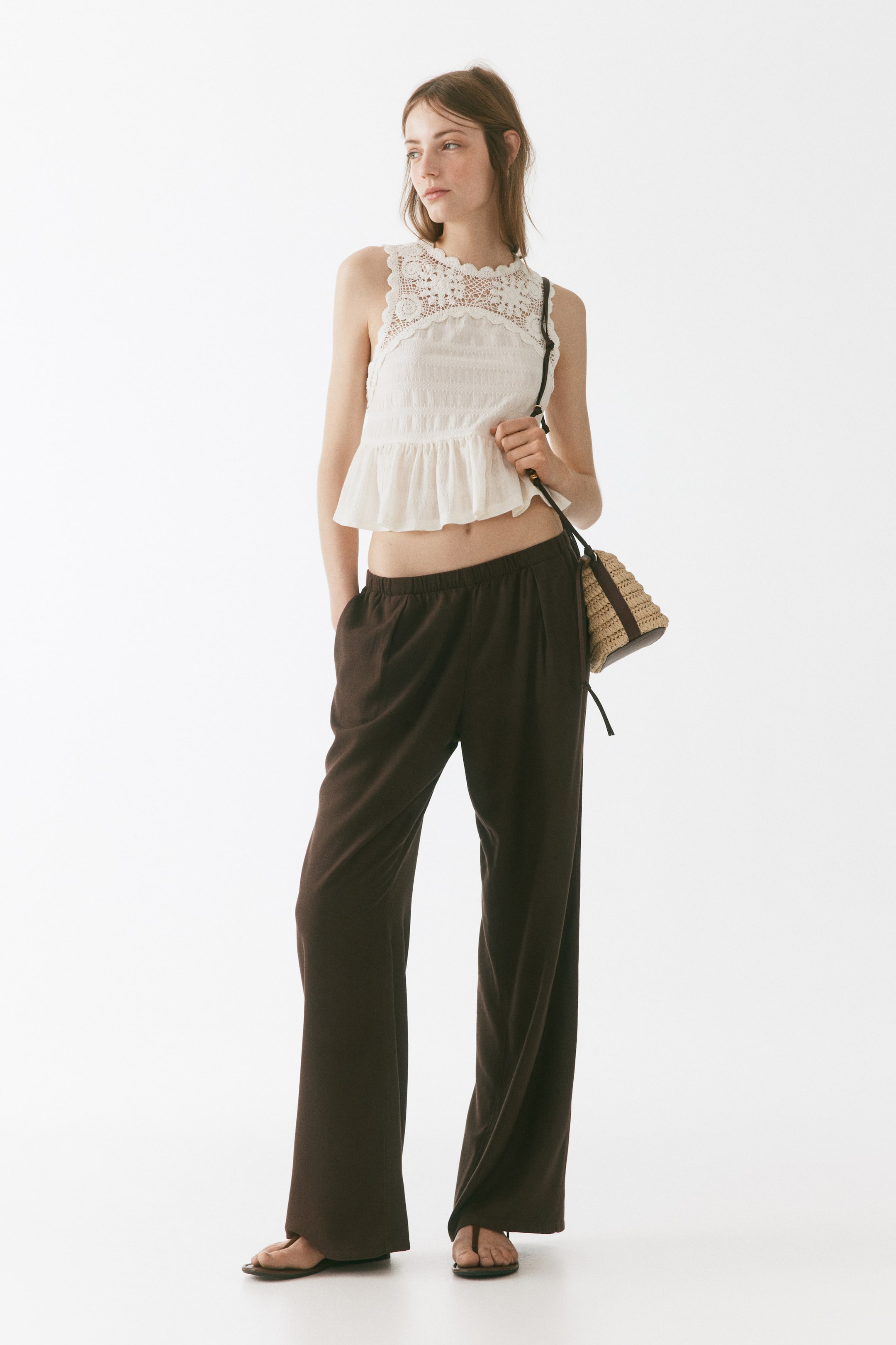 View larger image: A white sleeveless peplum top is showcasing a scalloped lace yoke and a gathered hem, while dark brown wide-leg pants are featuring an elastic waistband and a relaxed fit.