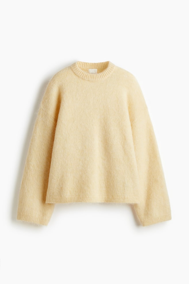 Un pull surdimensionné de couleur jaune clair est présenté de face, avec une texture tricotée douce et duveteuse. Il est conçu avec des épaules tombantes, des manches longues et est fini avec des bords côtelés au niveau de l'encolure ronde, des poignets et de l'ourlet. - 1