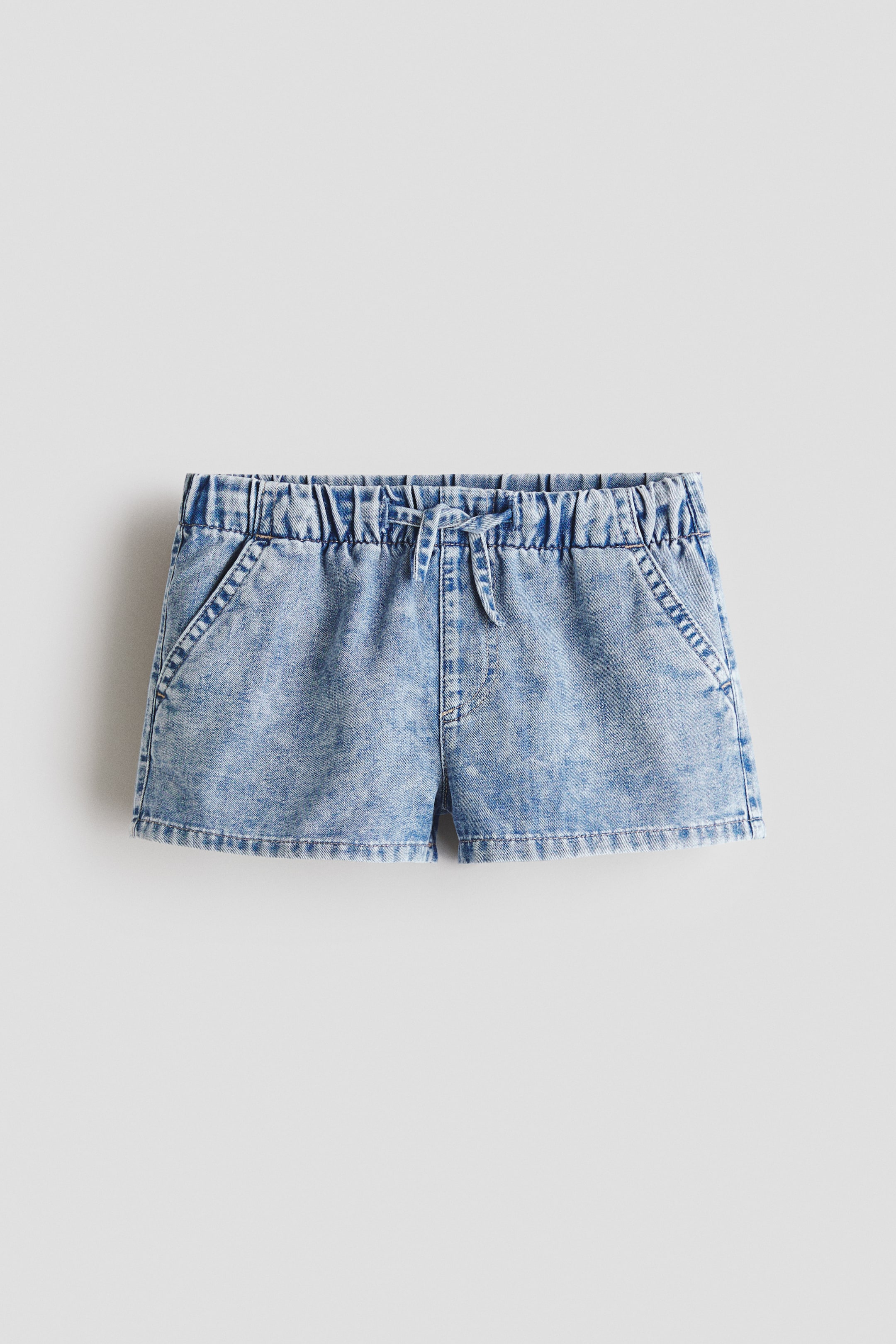View larger image: Denim shorts feature a light blue acid wash, an elastic waistband with a tied drawstring at the center front, and two angled slash pockets on the front.