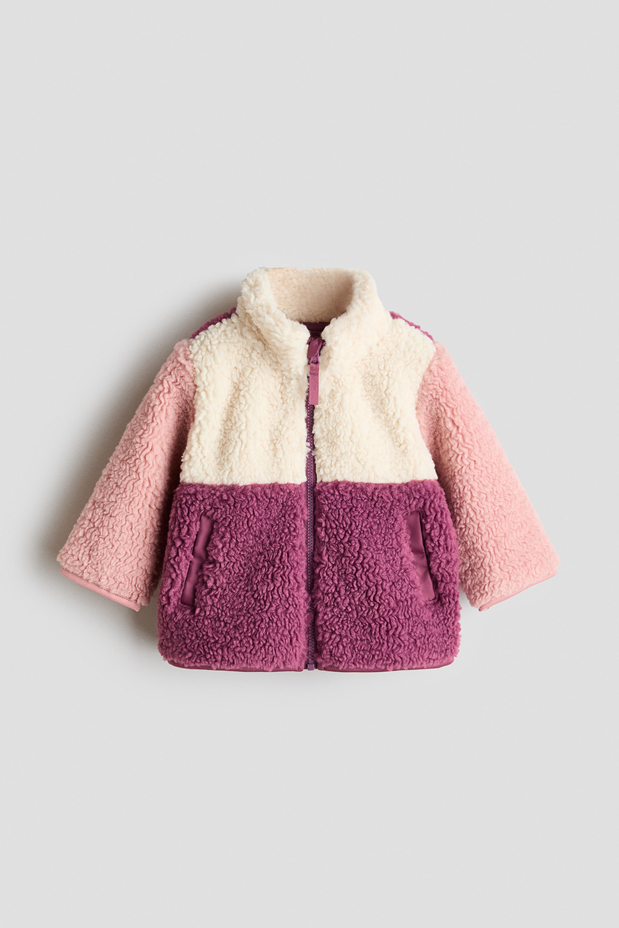 View larger image: A colour-blocked jacket displays its front view, crafted from soft teddy material. The stand collar and upper front are cream, the sleeves are light pink, and the lower front is dark pink. The jacket also features diagonal front pockets, a zip running down the front with an anti-chafe chin guard, and jersey bindings finishing the cuffs and hem.