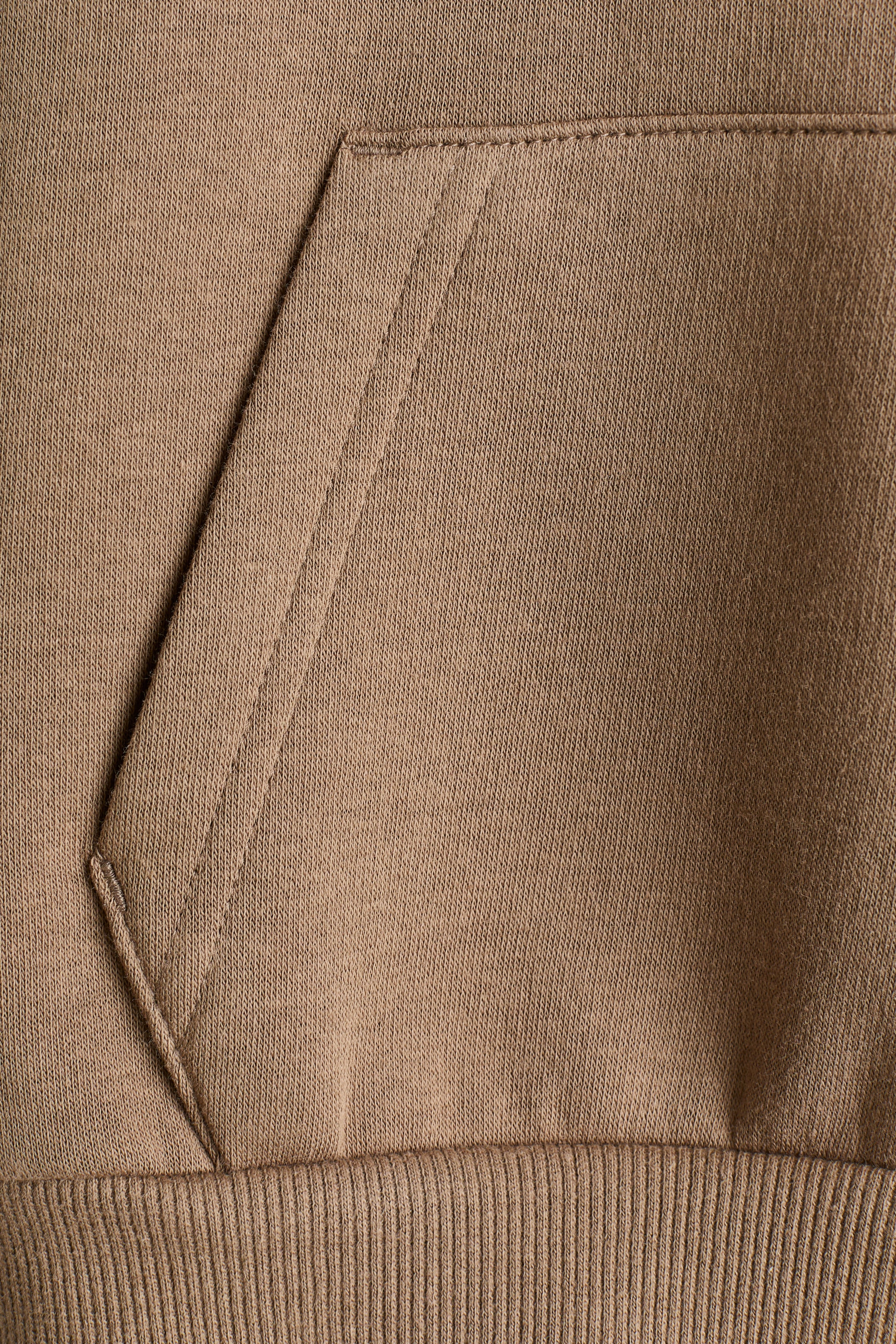 Größeres Bild anzeigen: Eine Nahaufnahme eines braunen Sweatshirts zeigt eine Kängurutasche und einen gerippten Saum.