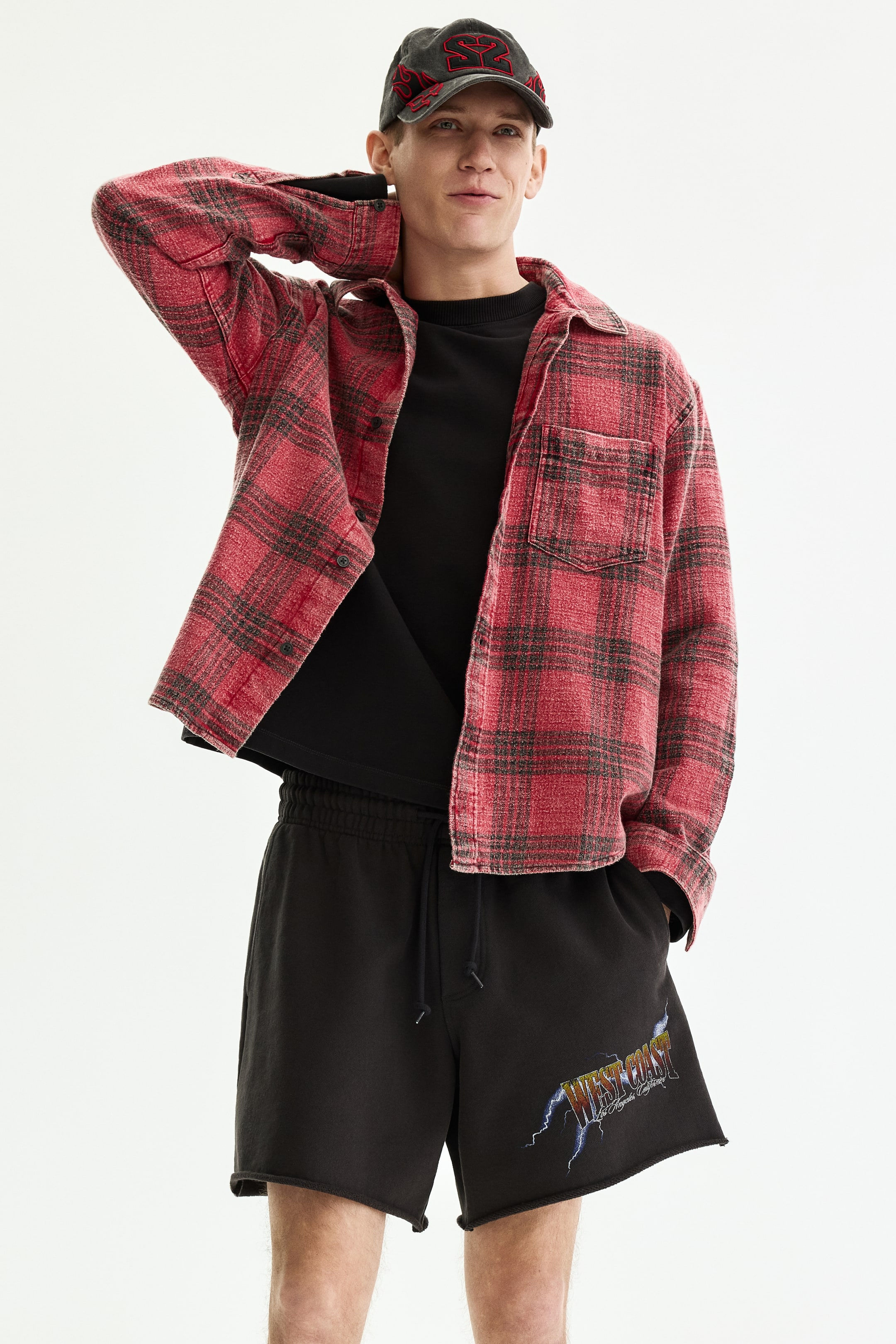 View larger image: A red and black plaid shirt is shown from the front, worn open over a black T-shirt. It features a pointed collar, long sleeves with buttoned cuffs, and a single patch pocket on the left chest.