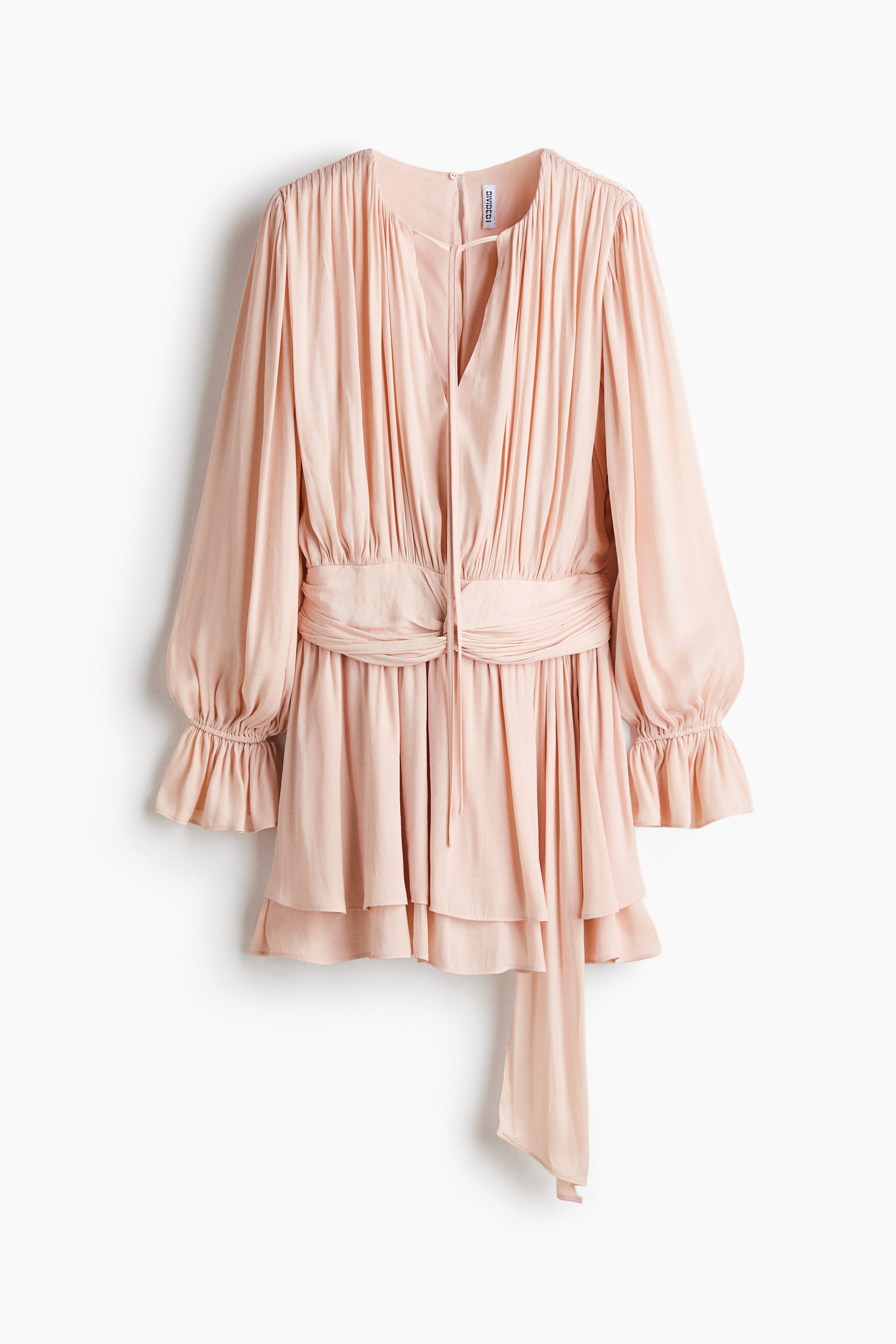 Ver imagen más grande: Un vestido corto de corte holgado en un tejido drapeado de color rosa claro presenta un escote redondo con una pequeña abertura y lazos estrechos en la PARTE DELANTERA. Cuenta con mangas largas con elástico por encima de los puños con volantes, una cintura drapeada con un detalle de nudo y un extremo largo, mientras que la falda aparece en capas.