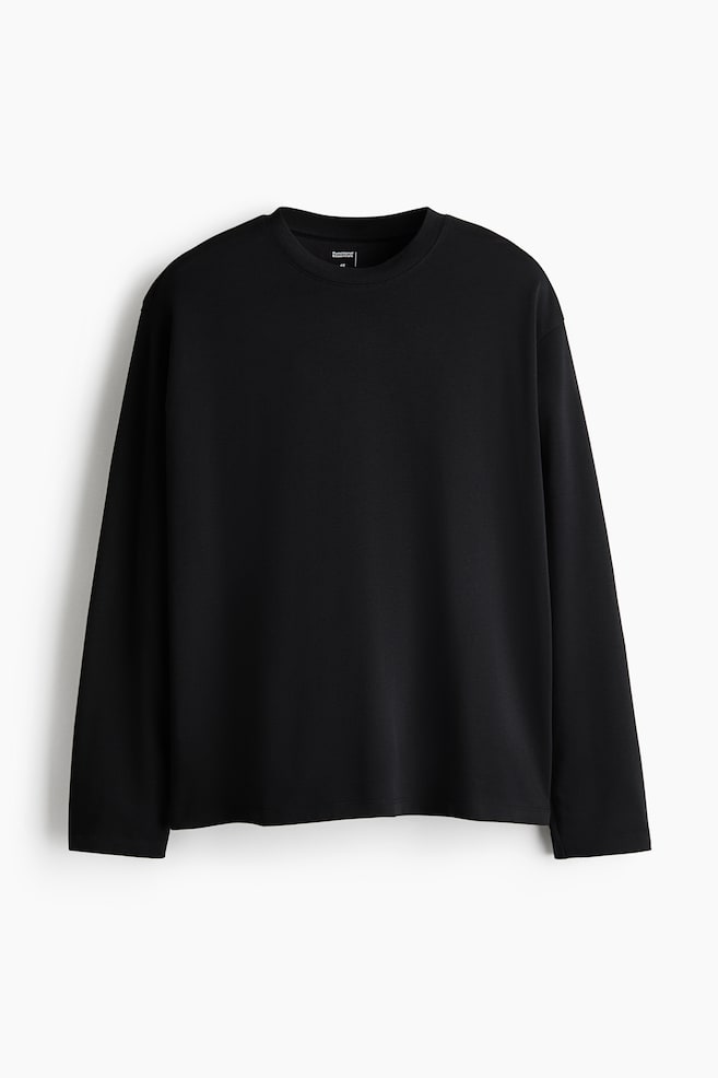 A black long-sleeved T-shirt is hanging front-on, showcasing a relaxed fit with a round neckline, dropped shoulders, and a straight-cut hem. - 1