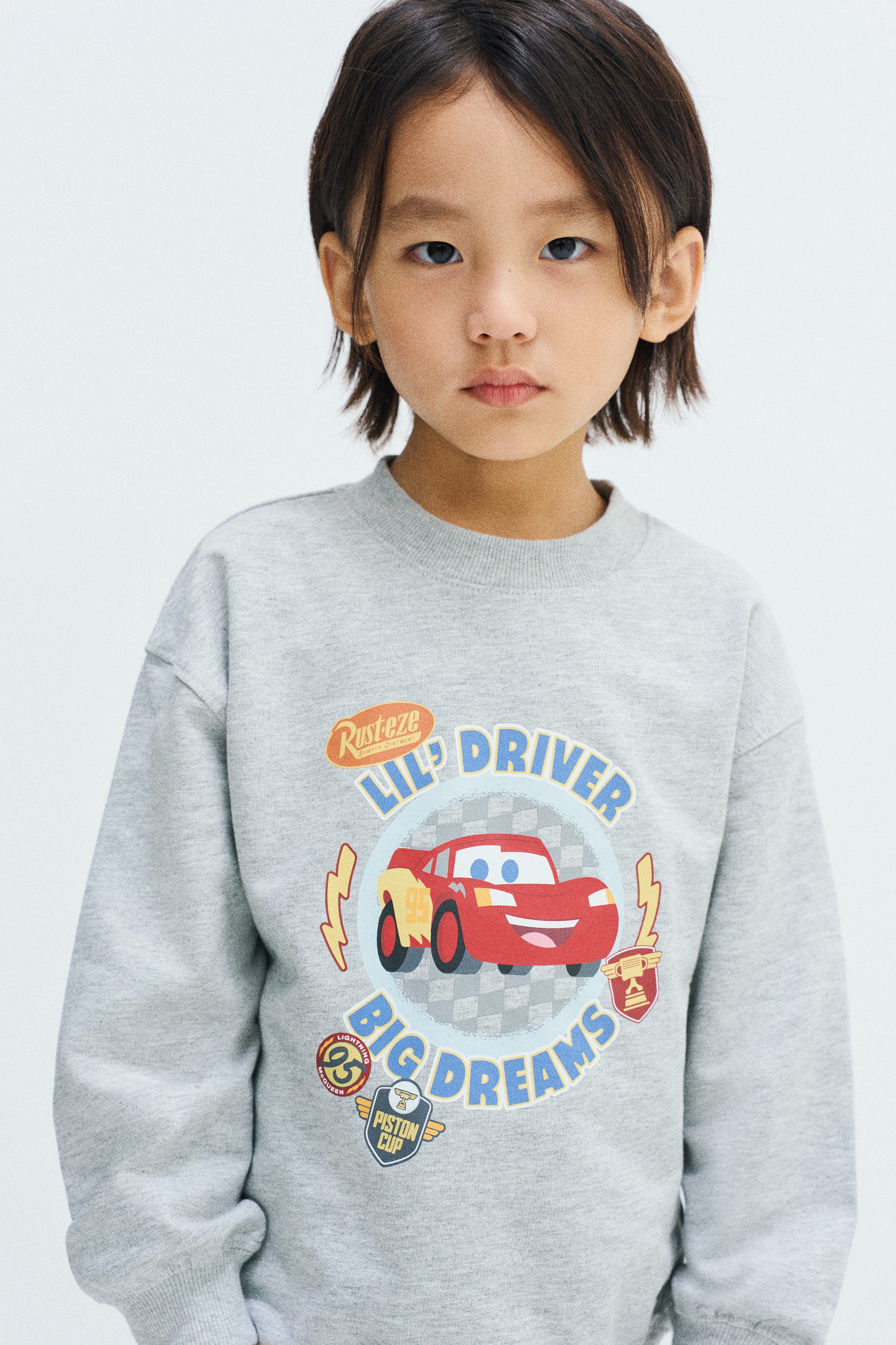 ã°ã¬ã¼ã®ã¹ã¦ã§ããã·ã£ãã¨ãæãã®ã¸ã§ã¬ã¼ãã³ãã®ã»ããããæ­£é¢åãã§è¡¨ç¤ºããã¦ãã¾ãããããã¹ã¯ããªãä»ä¸ãã®ã©ã¦ã³ãããã¯ã©ã¤ã³ããã­ããã·ã§ã«ãã¼ãä¸­å¤®ã«Lightning McQueenã®ã°ã©ãã£ãã¯ã¨ãLIL' DRIVER BIG DREAMSãã®ãã­ã¹ãããããã£ããã¶ã¤ã³ã§ããã³ã¼ãã£ãã¼ããããã¸ã§ã¬ã¼ãã³ãã¯ãè£¾ã®ã´ã ä»æ§ã¨ãå·¦ä¸è¿é¨åã«å°ããªãæãã®ã°ã©ãã£ãã¯ãæ½ããã¦ãã¾ãã