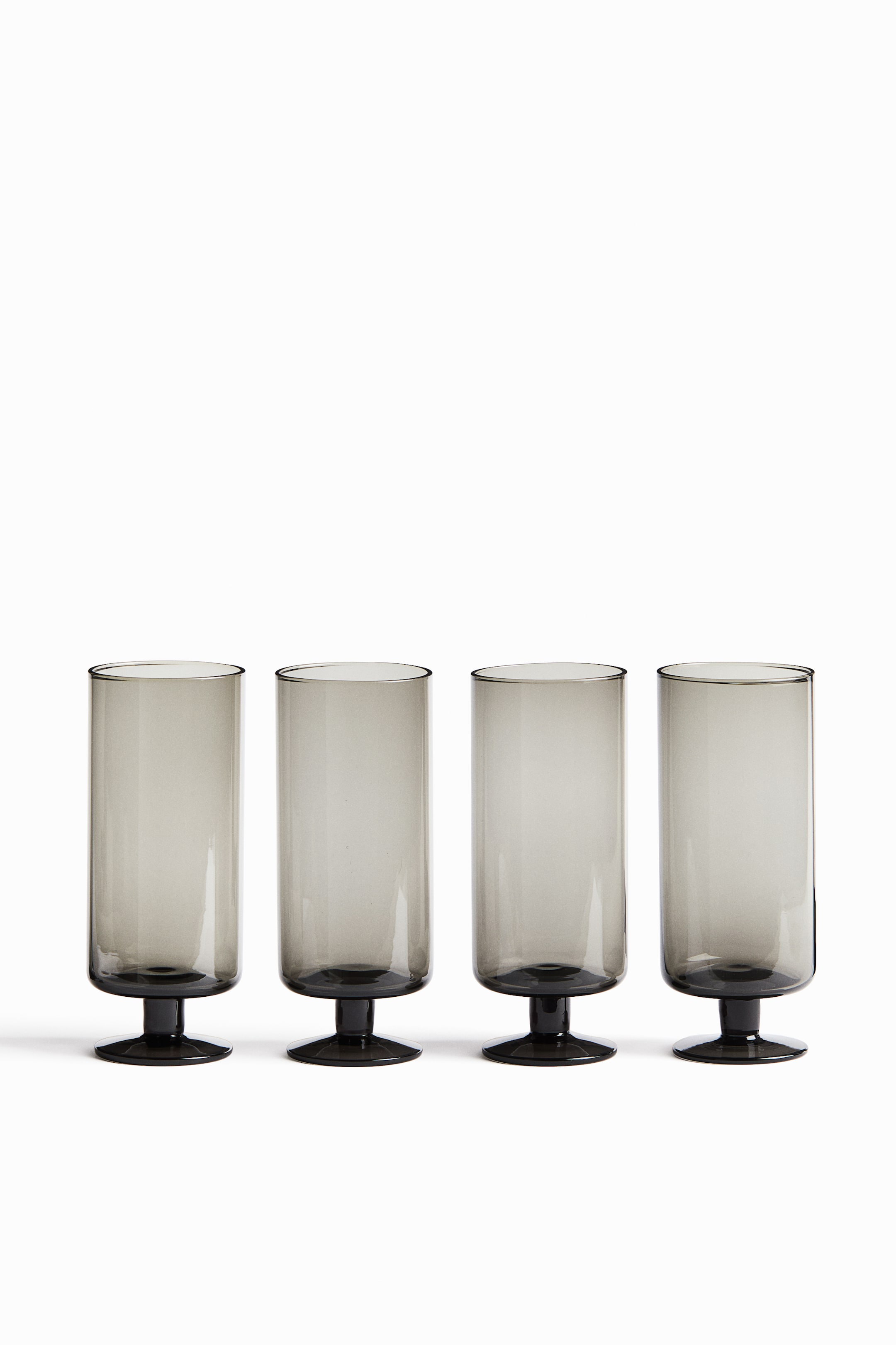 View larger image: Four mouth-blown, footed highball glasses in a translucent smoky gray hue are arranged in a horizontal row, facing forward. Each glass features a straight-sided cylindrical body supported by a short, thick stem and a flat circular base.
