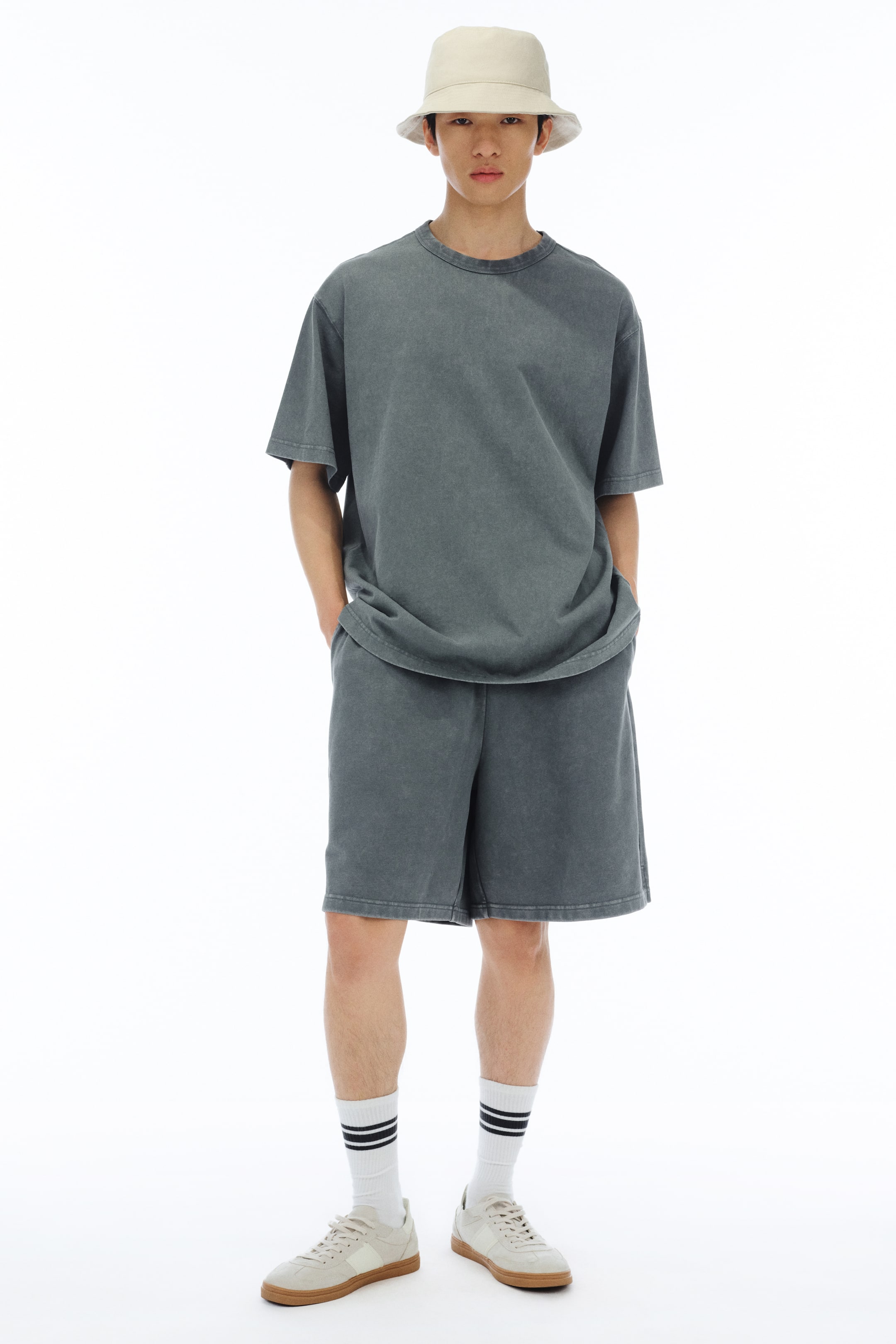 View larger image: The model is sporting a soft beige bucket hat, featuring a gently rounded crown and a short brim.