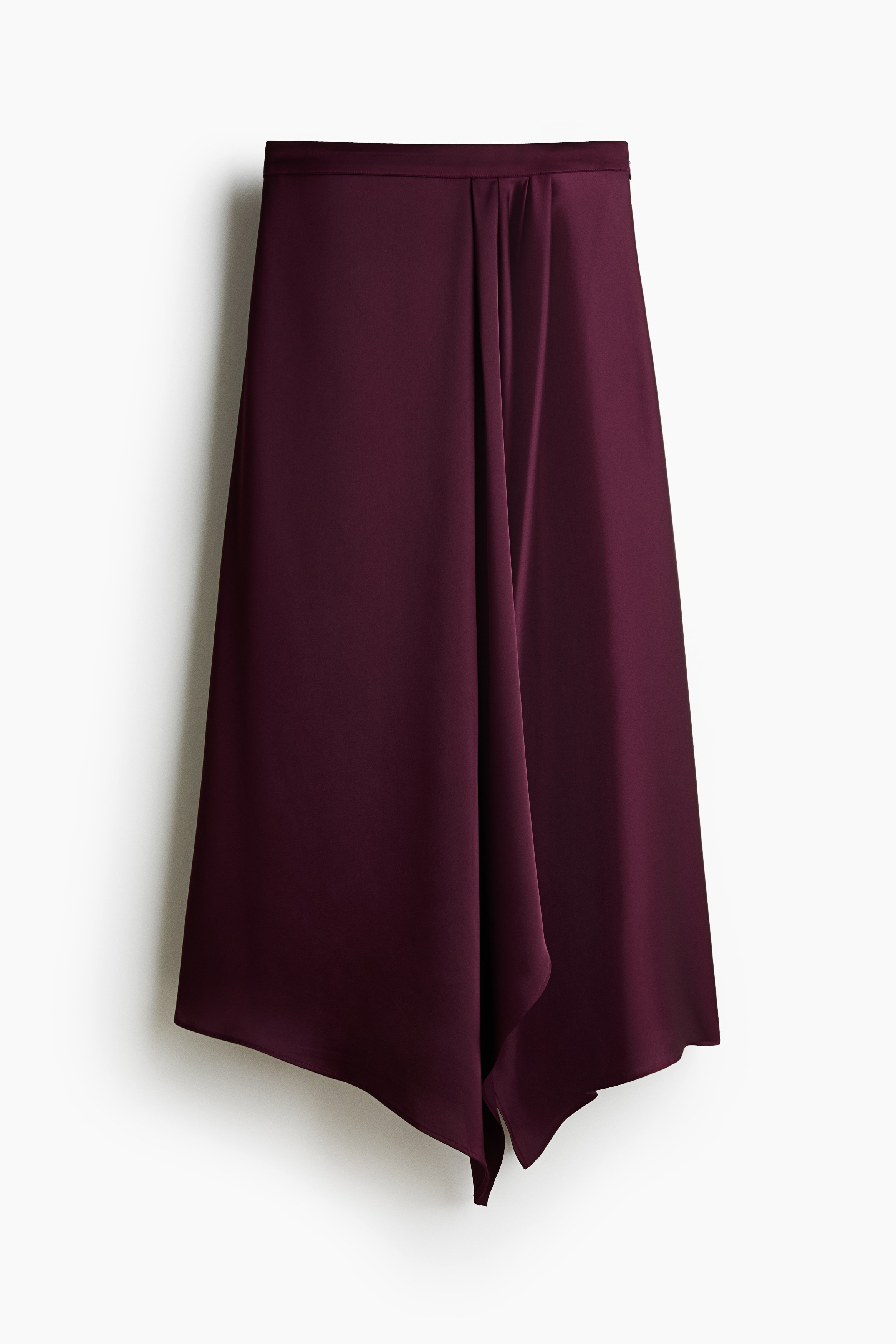 A calf-length, high-waisted satin skirt in dark burgundy is being worn by the model, paired with a black tank top. The skirt features a loose fit with a draped panel on the side and an asymmetrical handkerchief hem.