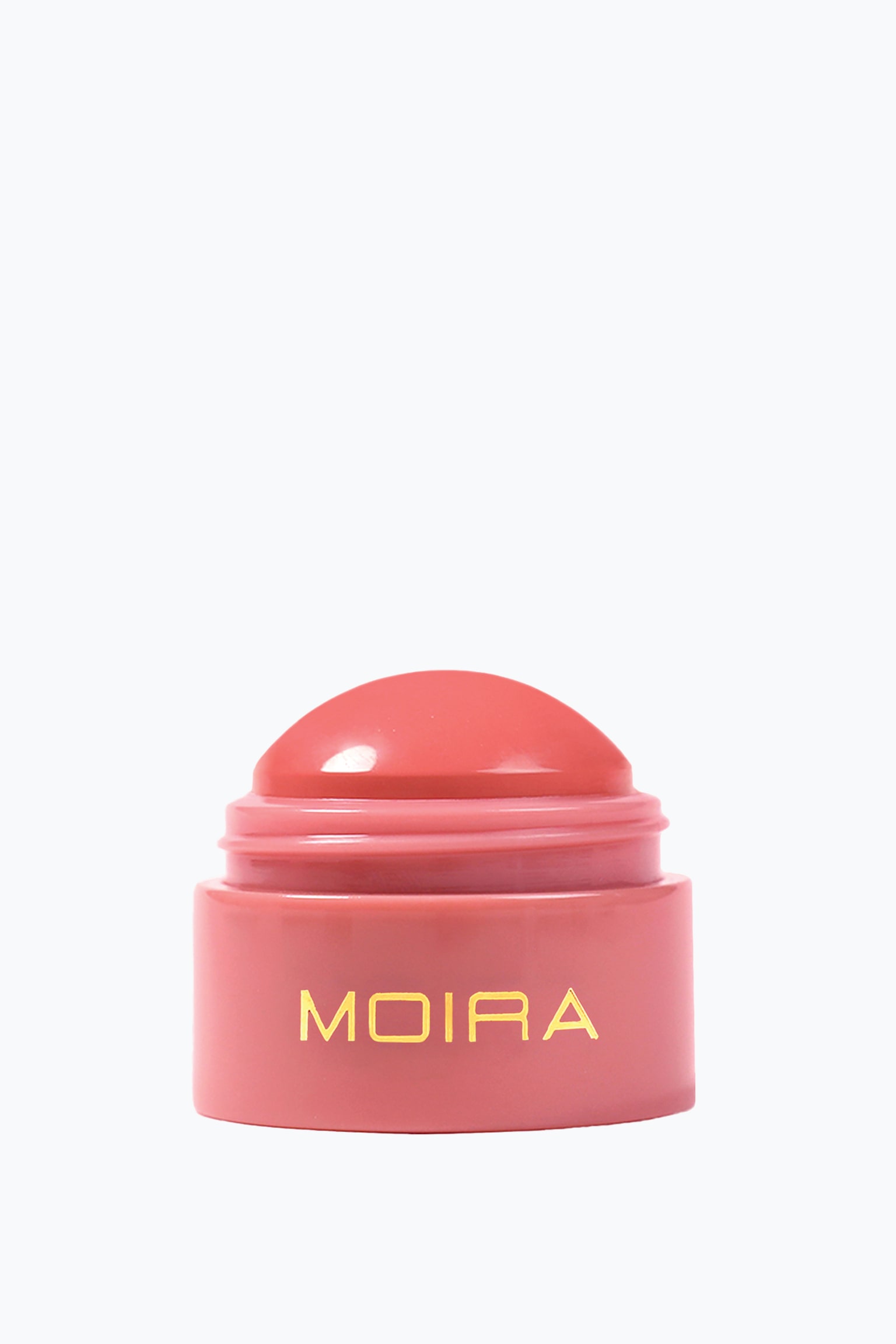 Ett krÃ¤mrouge i balmform stÃ¥r upprÃ¤tt och visar upp en slÃ¤t, kupolformad korallrosa produkt som sticker upp ur en matchande rosa cylindrisk bas. Framsidan av behÃ¥llaren visar varumÃ¤rket "MOIRA" i gyllene versaler. - 1