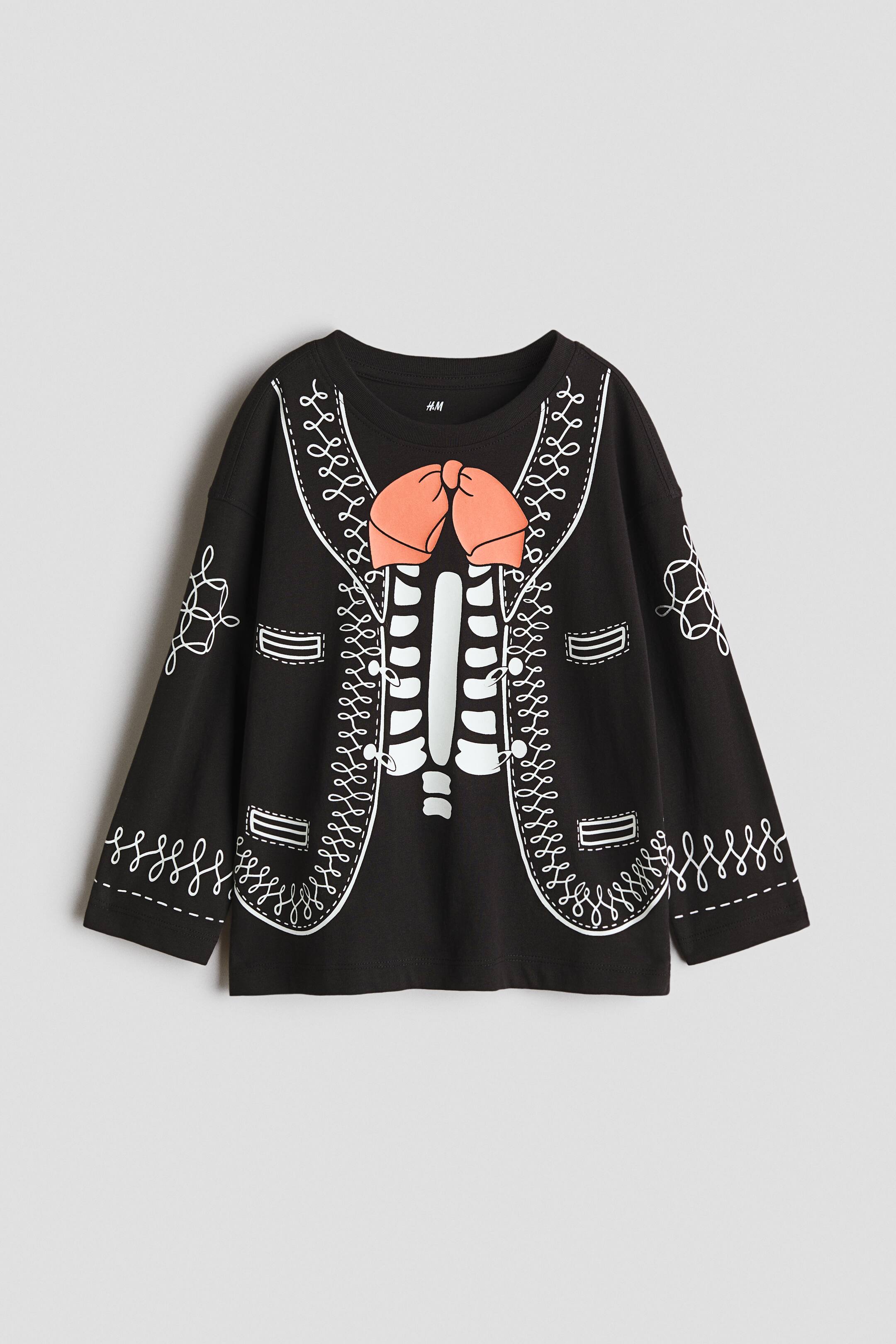 View larger image: A black long-sleeved shirt is laid flat, facing forward, showcasing a white skeleton rib cage print down the center. An orange bow tie is printed above the skeleton, with white scrollwork patterns mimicking a jacket's lapels, pockets, and sleeve embroidery.
