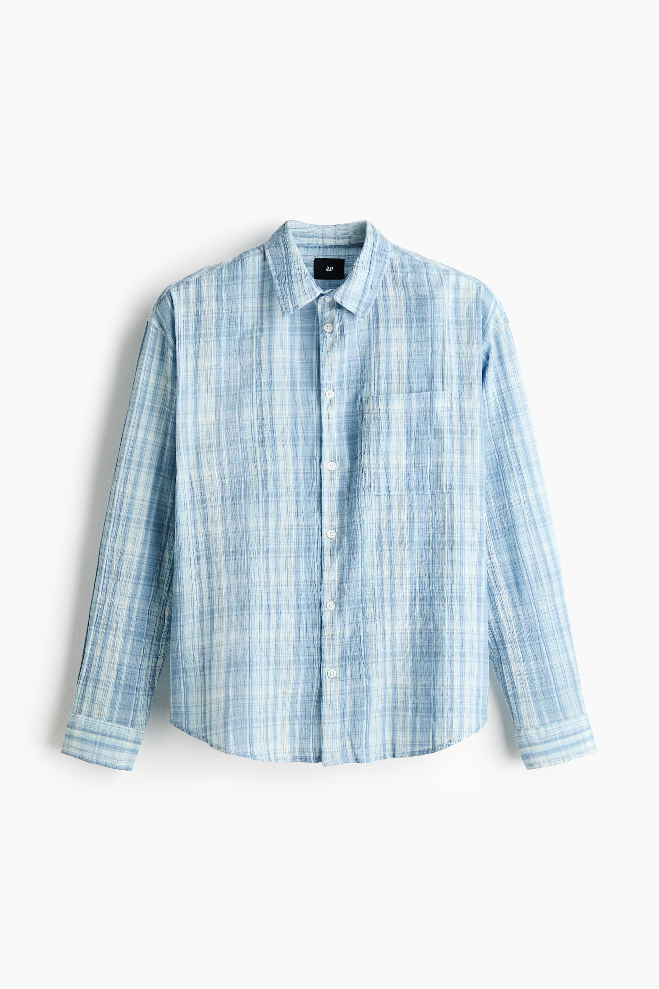 View larger image: A light blue and white checkered shirt is hanging, facing front. It showcases a crinkled texture, a standard collar, a full-button placket with white buttons, and a single patch pocket on the left chest. The long sleeves end in buttoned cuffs.