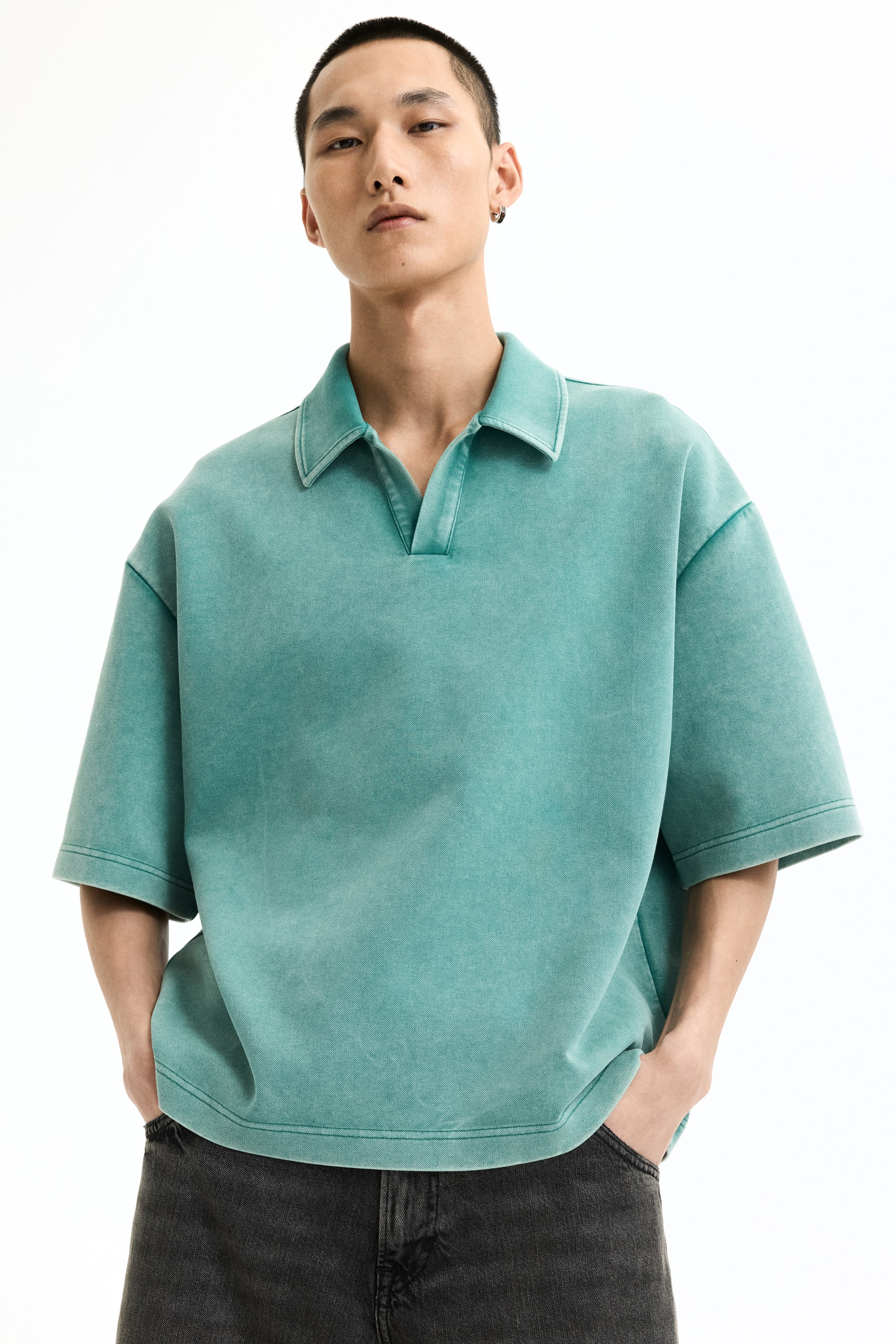 View larger image: A washed teal polo shirt featuring a spread collar and a V-neck opening, presented with a relaxed fit and short, wide sleeves. It showcases a straight hem and visible stitching details.