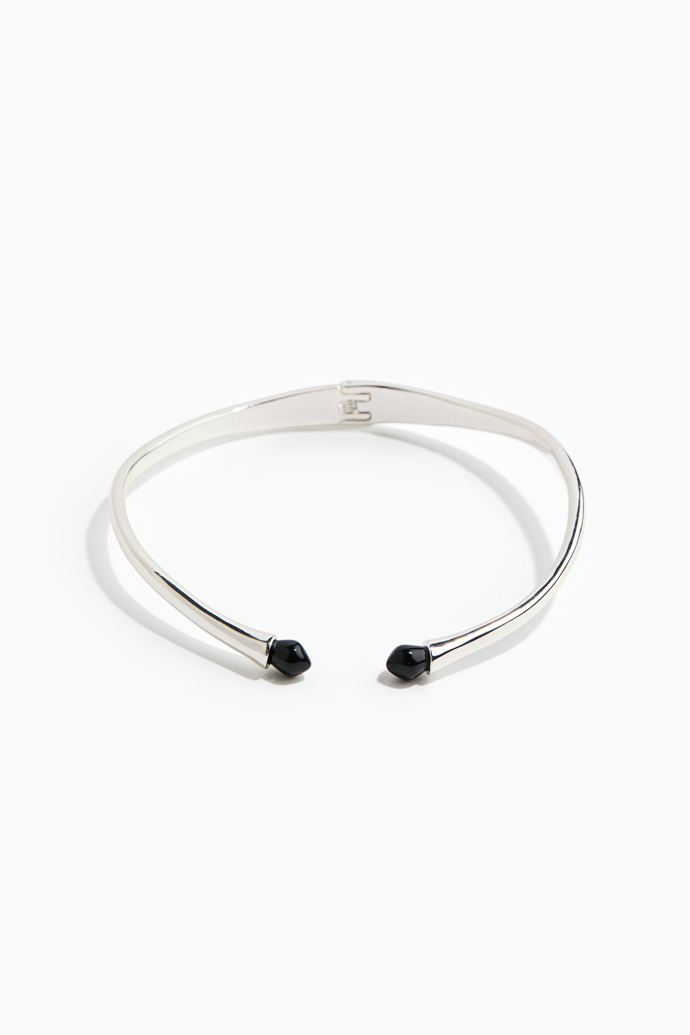 A rigid, silver-toned metal choker necklace featuring contrasting black resin beads at its open front ends is worn by the model. The necklace sits on the collarbone and is styled with a black scoop-neck top.