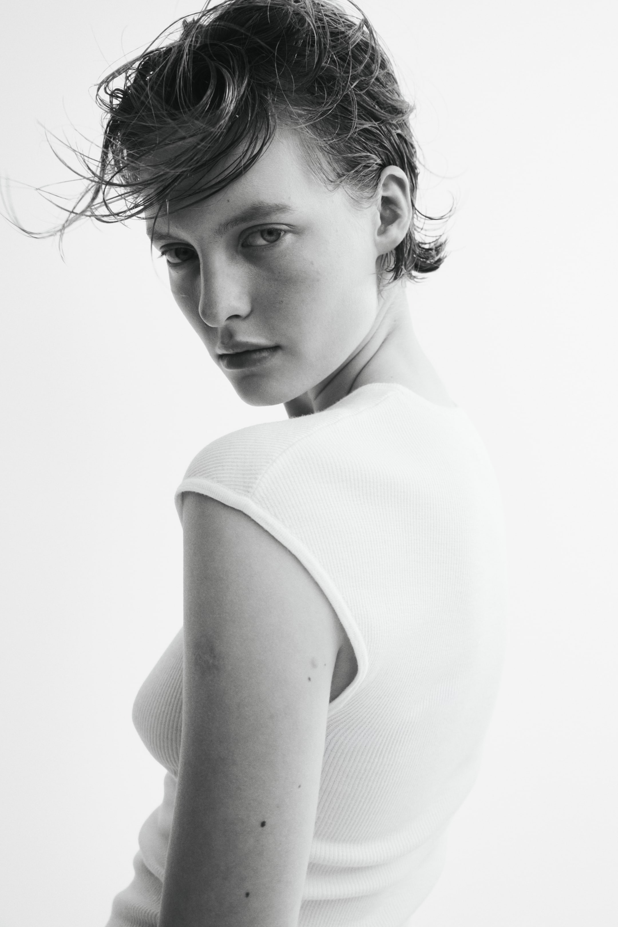 View larger image: The model is wearing a fitted ribbed knit top. The top features a round neckline and cap sleeves.