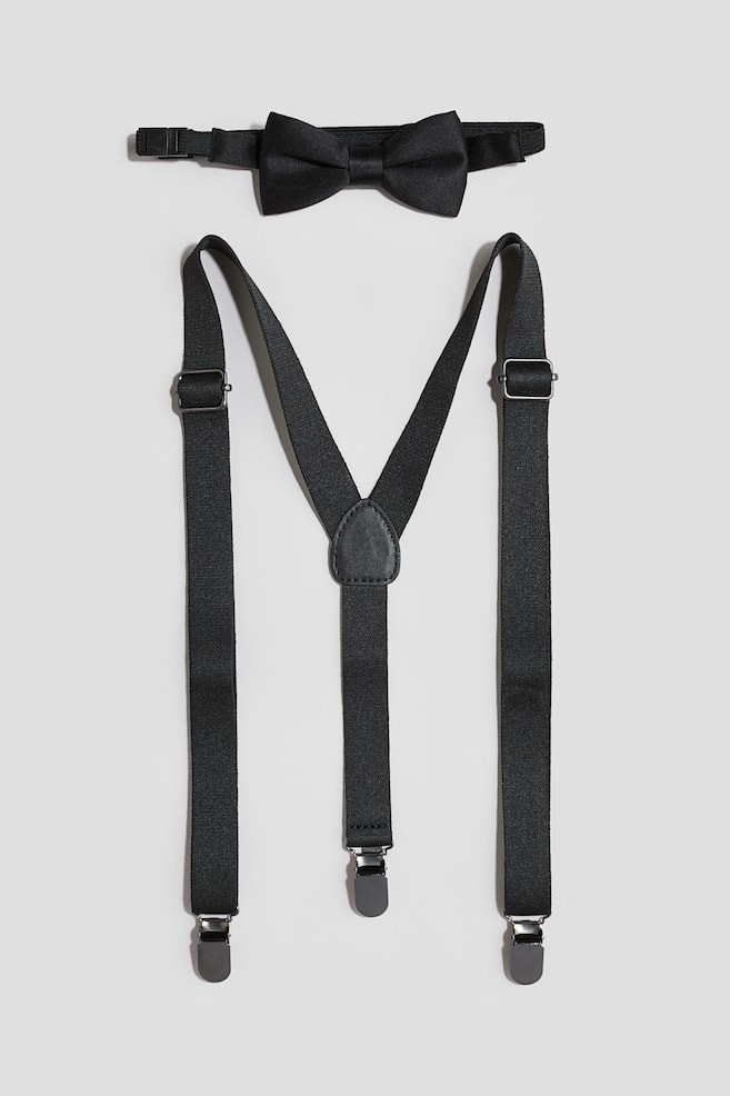 Un ensemble dâaccessoires noirs comprenant un nÅud papillon prÃ©-nouÃ© et des bretelles assorties en Y est prÃ©sentÃ© Ã  plat, en vue de face. Le nÅud papillon en satin laisse apparaÃ®tre une bride de cou rÃ©glable, tandis que les bretelles affichent des rÃ©glages coulissants en mÃ©tal argentÃ©, une piÃ¨ce centrale effet cuir et trois attaches mÃ©talliques Ã  clip. - 1