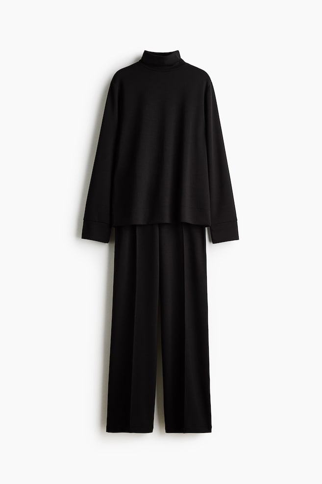 A black jersey set is shown from the front, featuring a long-sleeved top with a stand collar layered over matching straight-leg trousers with stitched creases down the front. - 1