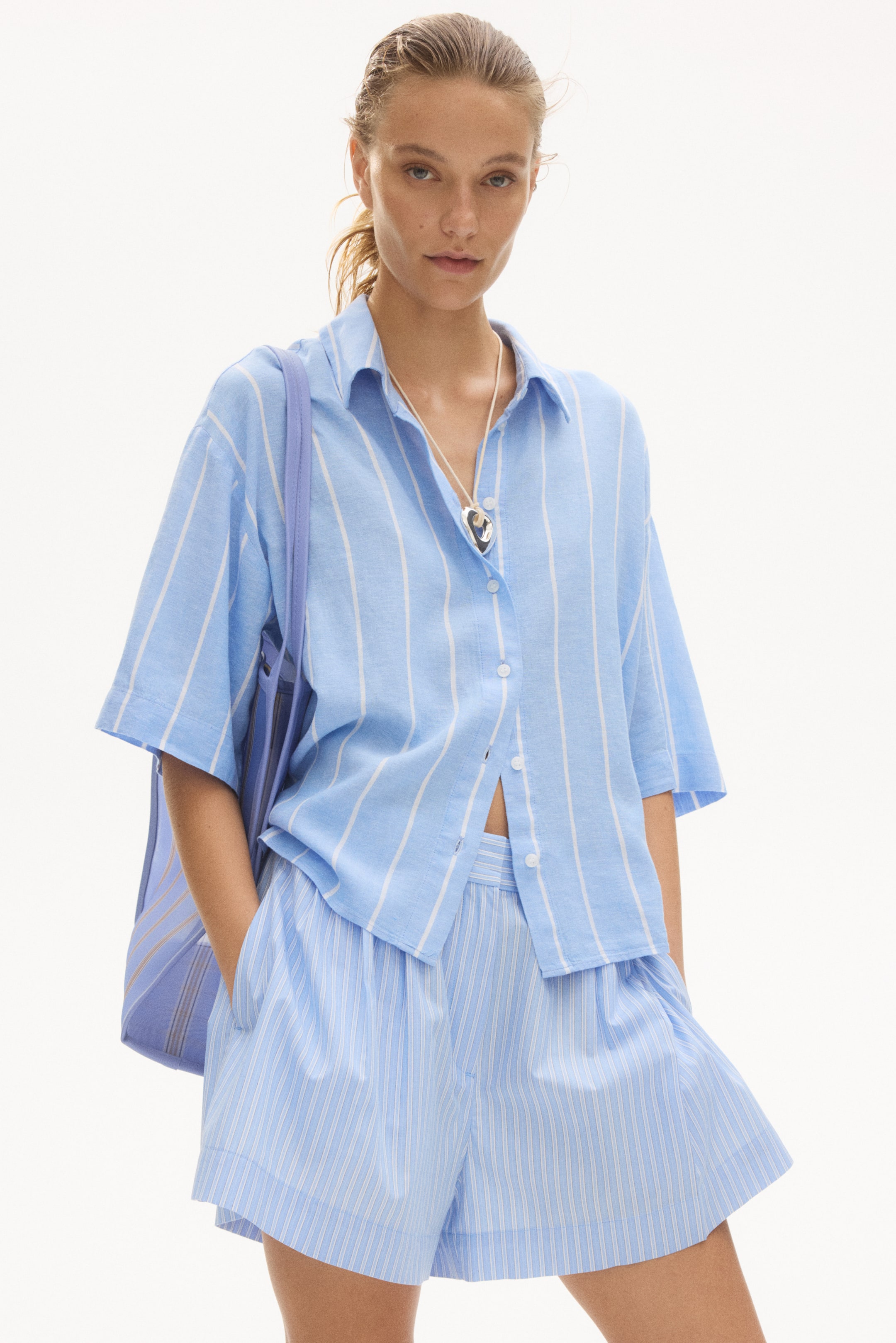 View larger image: Loose-fit shorts in a light blue hue adorned with subtle white vertical stripes, showcasing a high-waist design, front pleats, and discreet side pockets when viewed from the front.