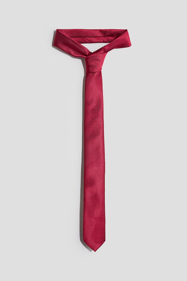 A classic tie in a dark pink woven fabric is lying flat and facing front, showcasing its fine diagonal ribbed texture. The tie features a narrow width, a neat knot, and a pointed tip. - 1
