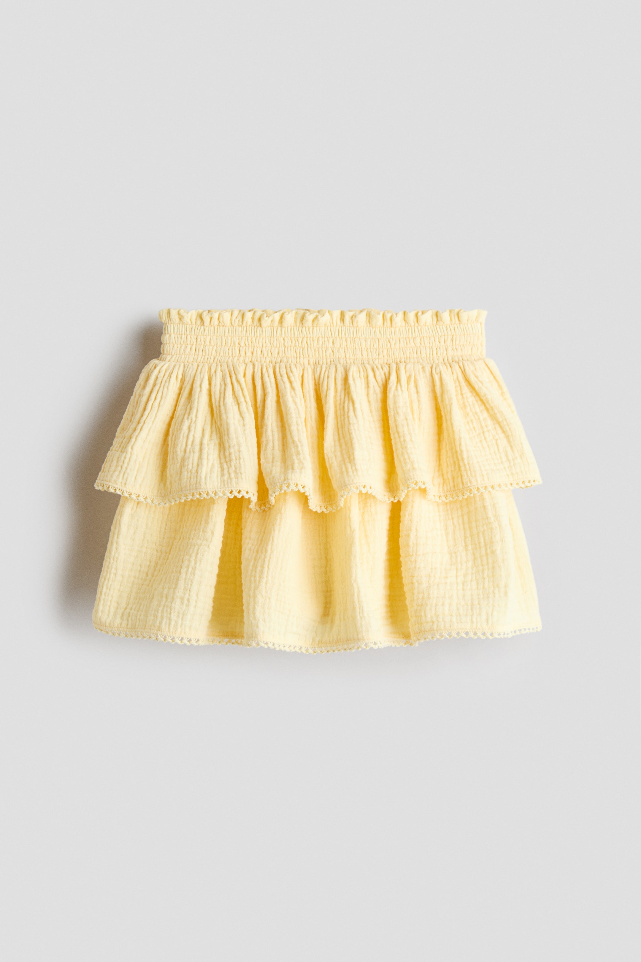 Ver imagem maior: Uma saia amarela em camadas de musselina de algodão macio é apresentada de frente. Apresenta uma cintura franzida com um acabamento de folho estreito e duas camadas, cada uma exibindo bordas com acabamento em picot.