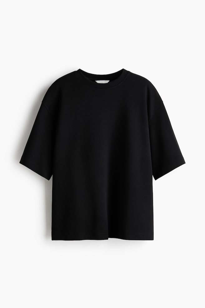 Een zwart t-shirt toont zijn voorkant met een ronde hals en korte, wijde mouwen. Het heeft een losse, ontspannen pasvorm. - 1