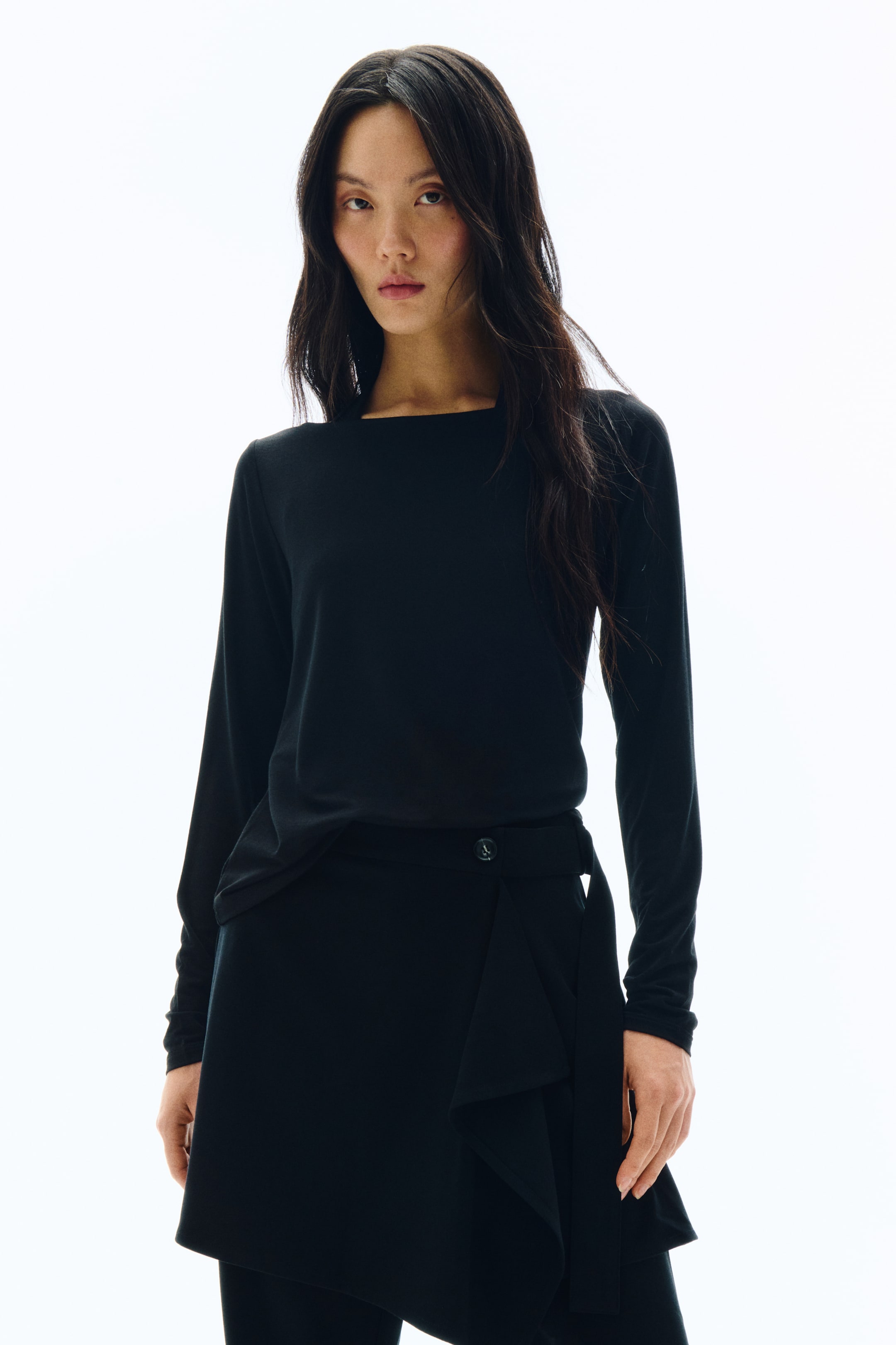 拡大画像を表示: ブラックの長袖トップス。ワイドなボートネックライン、フィット感のあるロングスリーブ、そしてボディラインをゆるやかに包み込むリラックスしたドレープ感が特徴です。