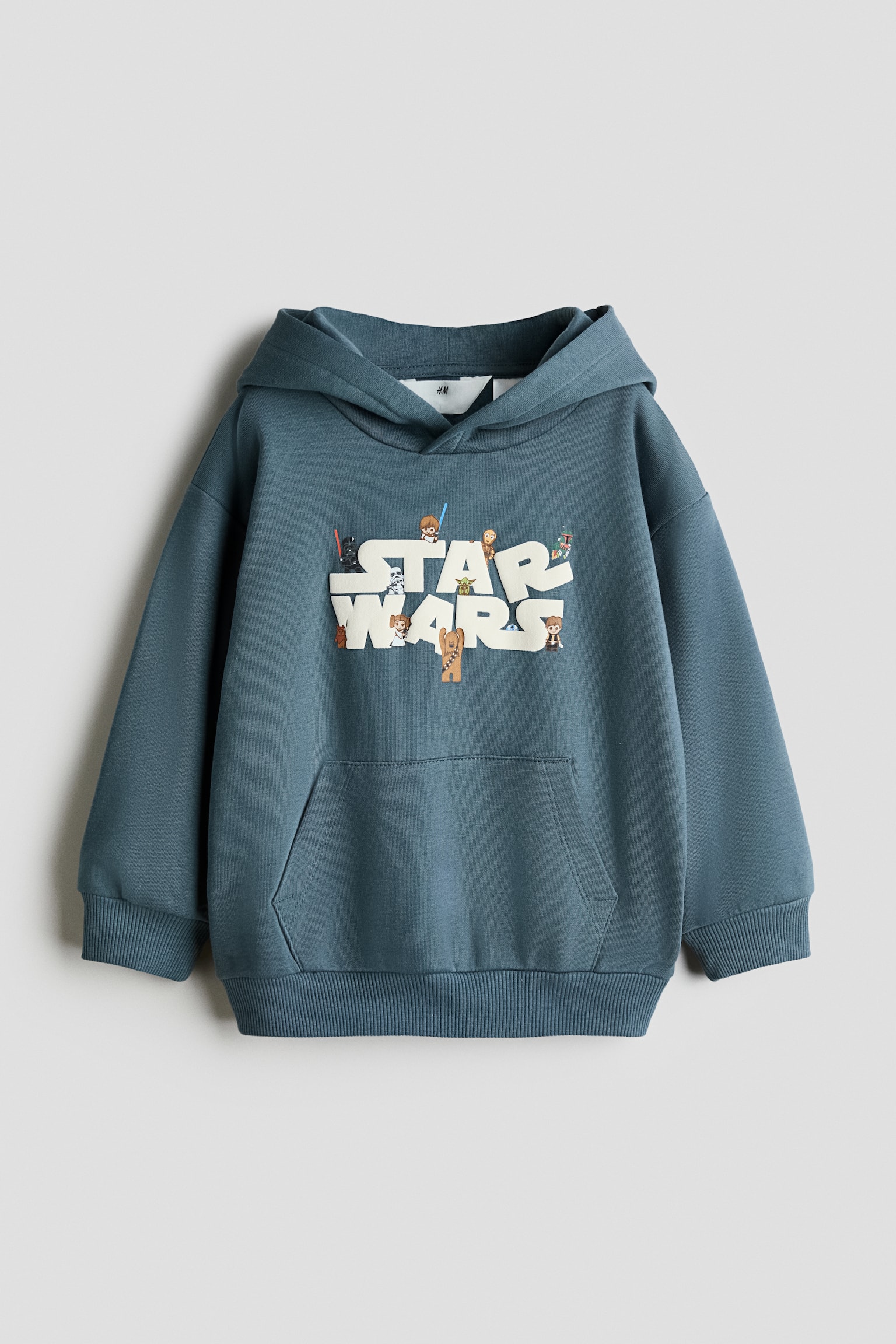 A loose-fit blue hoodie is shown from the front, featuring a wrap-front hood, dropped shoulders, and a front kangaroo pocket. The chest is displaying a printed "Star Wars" graphic in large white letters adorned with small cartoon characters, finished with ribbed cuffs and a ribbed hem.
