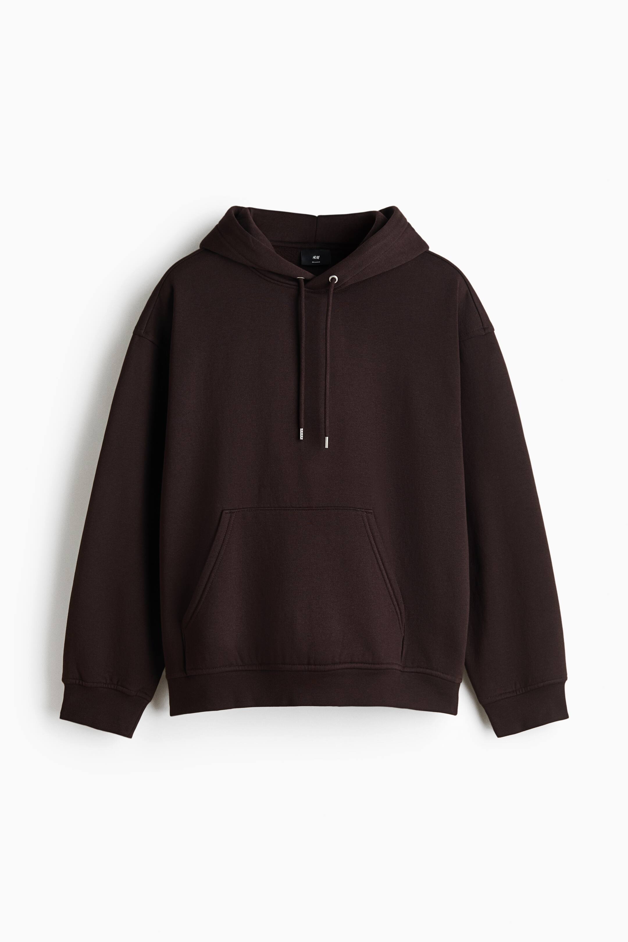 View larger image: A dark brown hoodie is shown from the front, featuring a drawstring hood, dropped shoulders, and a kangaroo pocket. The garment includes long sleeves with ribbed cuffs and a wide ribbed hem, presenting a loose and relaxed silhouette.