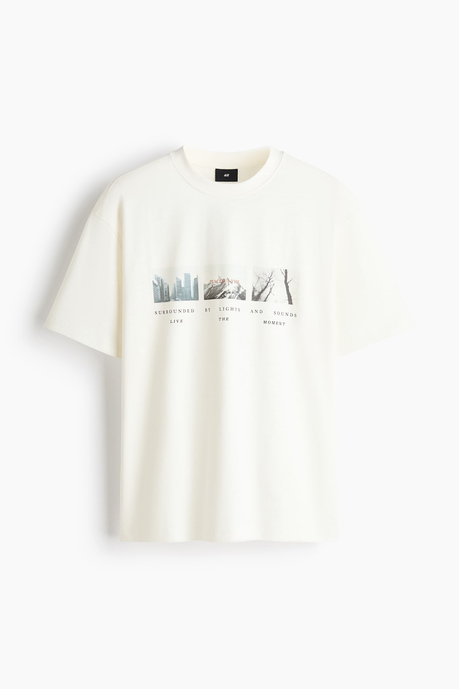 An off-white, heavyweight cotton jersey t-shirt is shown from the front, featuring a loose fit, dropped shoulders, and a round, rib-trimmed neckline. The chest is displaying a graphic print of three small square photographs depicting a skyline, mountains, and trees, with black printed text underneath. - 1