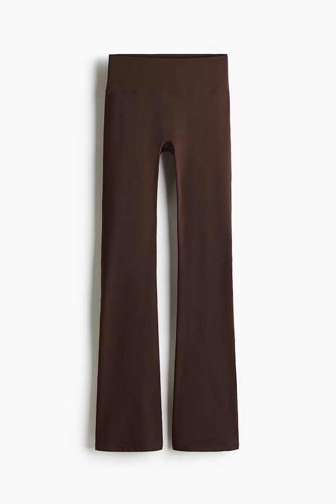 Flared sports leggings are presented from the FRONT, featuring a solid dark brown color, a wide high-rise waistband, and legs that are fitted through the thigh before flaring widely from the knee to the hem. - 1