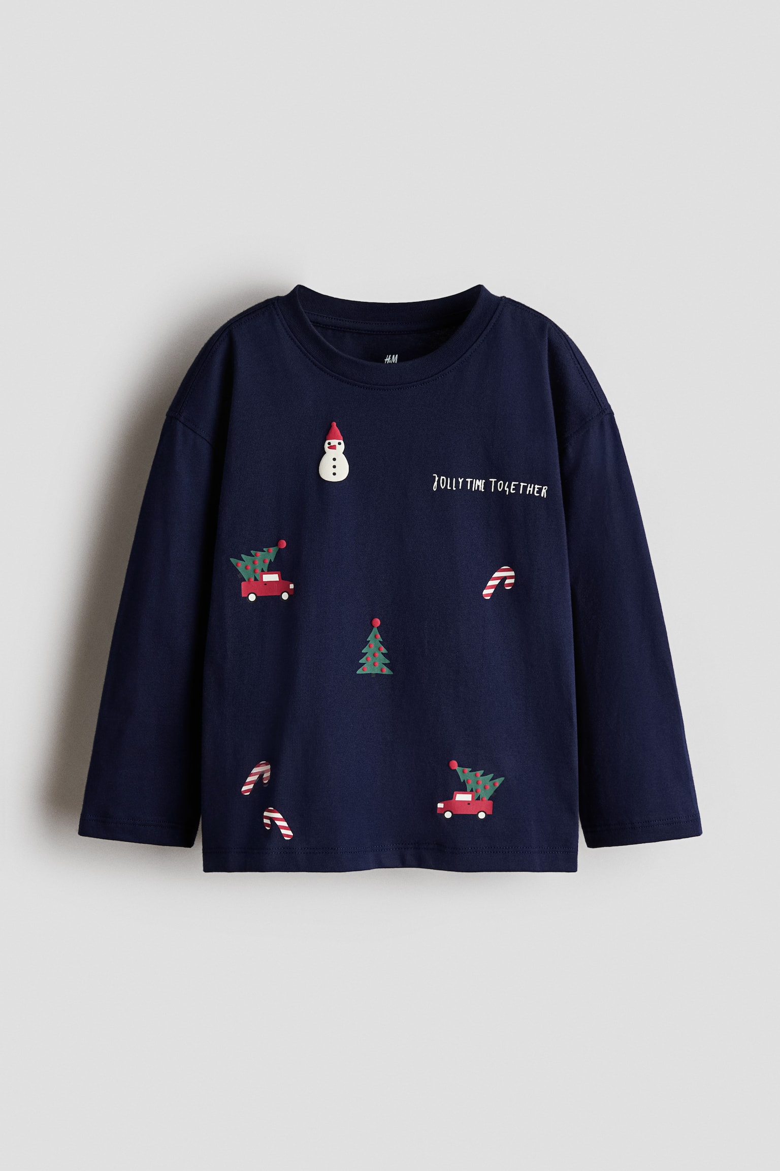 Vue de face dâun t-shirt Ã  manches longues bleu marine en jersey de coton, prÃ©sentant un col rond avec bordure soulignÃ©e et des Ã©paules tombantes. Lâavant affiche un motif imprimÃ© composÃ© de motifs de NoÃ«l Ã©pars tels quâun bonhomme de neige, des cannes en sucre dâorge, des sapins de NoÃ«l dÃ©corÃ©s, des camionnettes rouges et le texte Â« JOLLY TIME TOGETHER Â» en Ã©criture blanche.