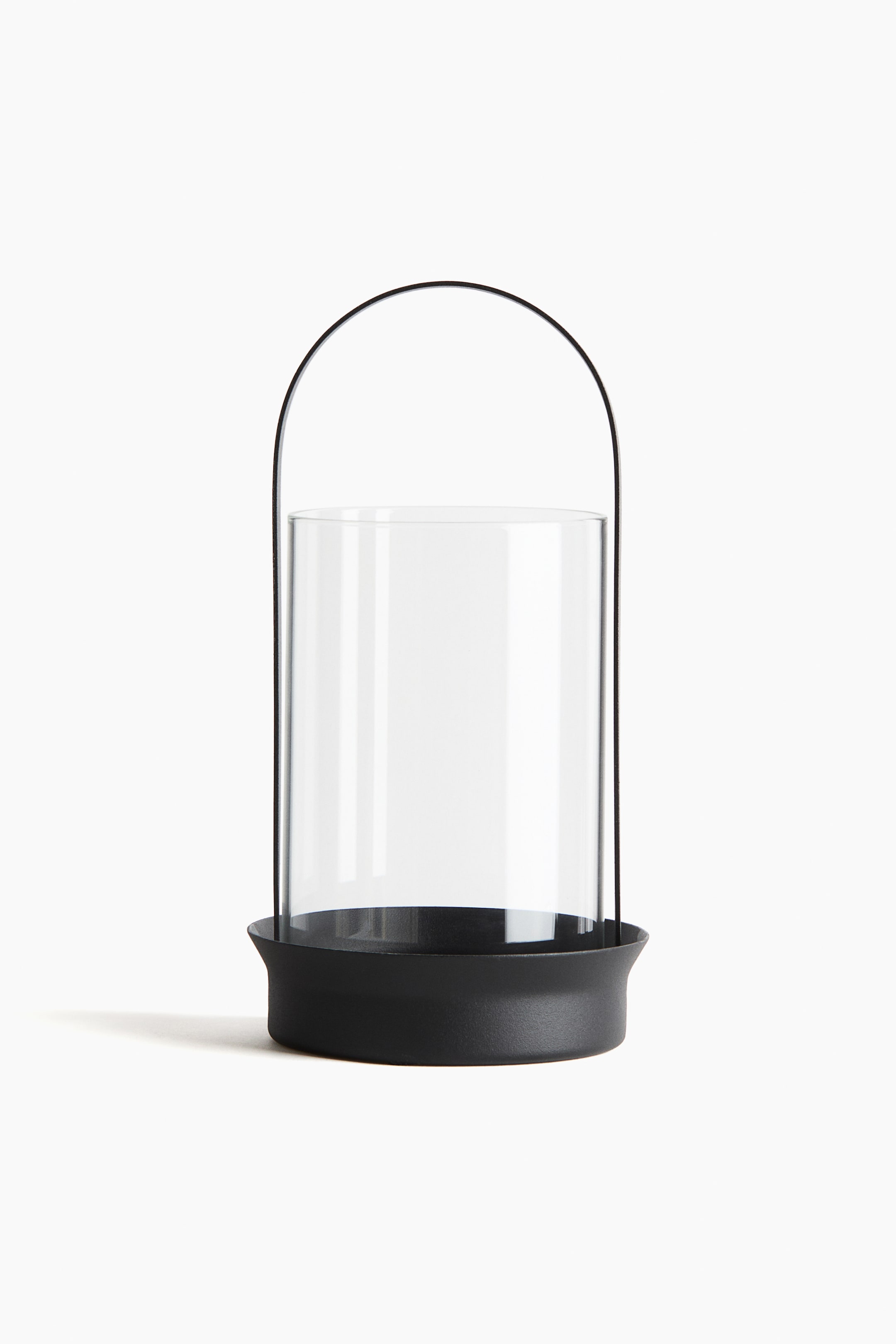 View larger image: A front-facing lantern is presenting a clear cylindrical glass insert, which is resting within a matte black base featuring a slightly flared rim.